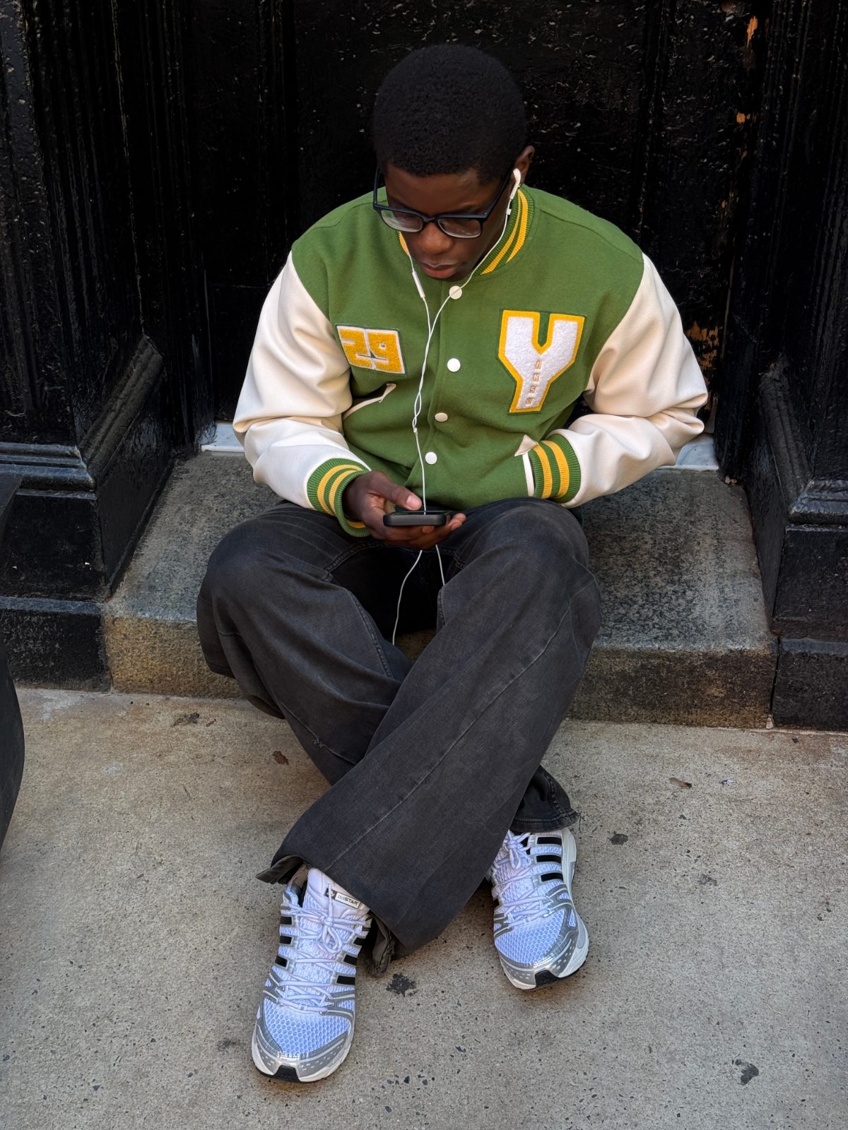 Green and white letterman jacket, dark wash jeans, white and silver sneakers.