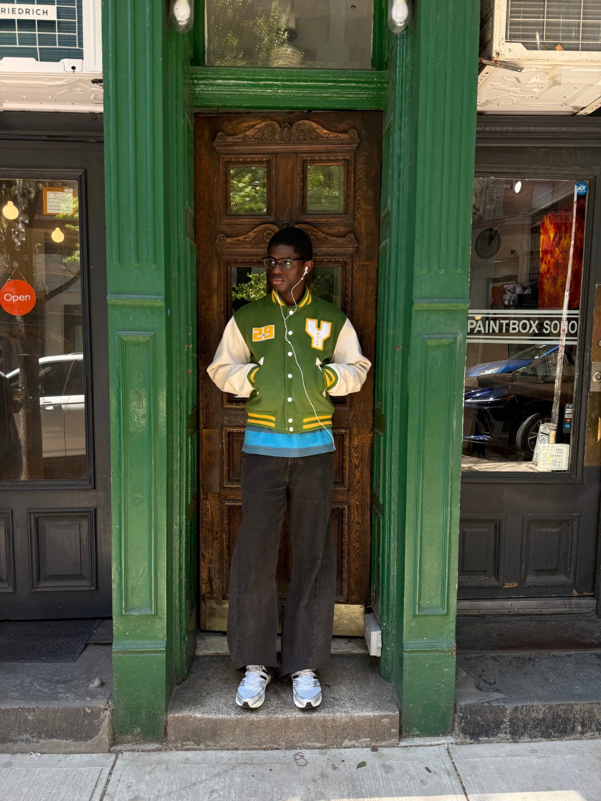 reen-and-white letterman jacket over a bright blue base layer, pairing it with relaxed charcoal trousers and silver metallic adidas running sneakers