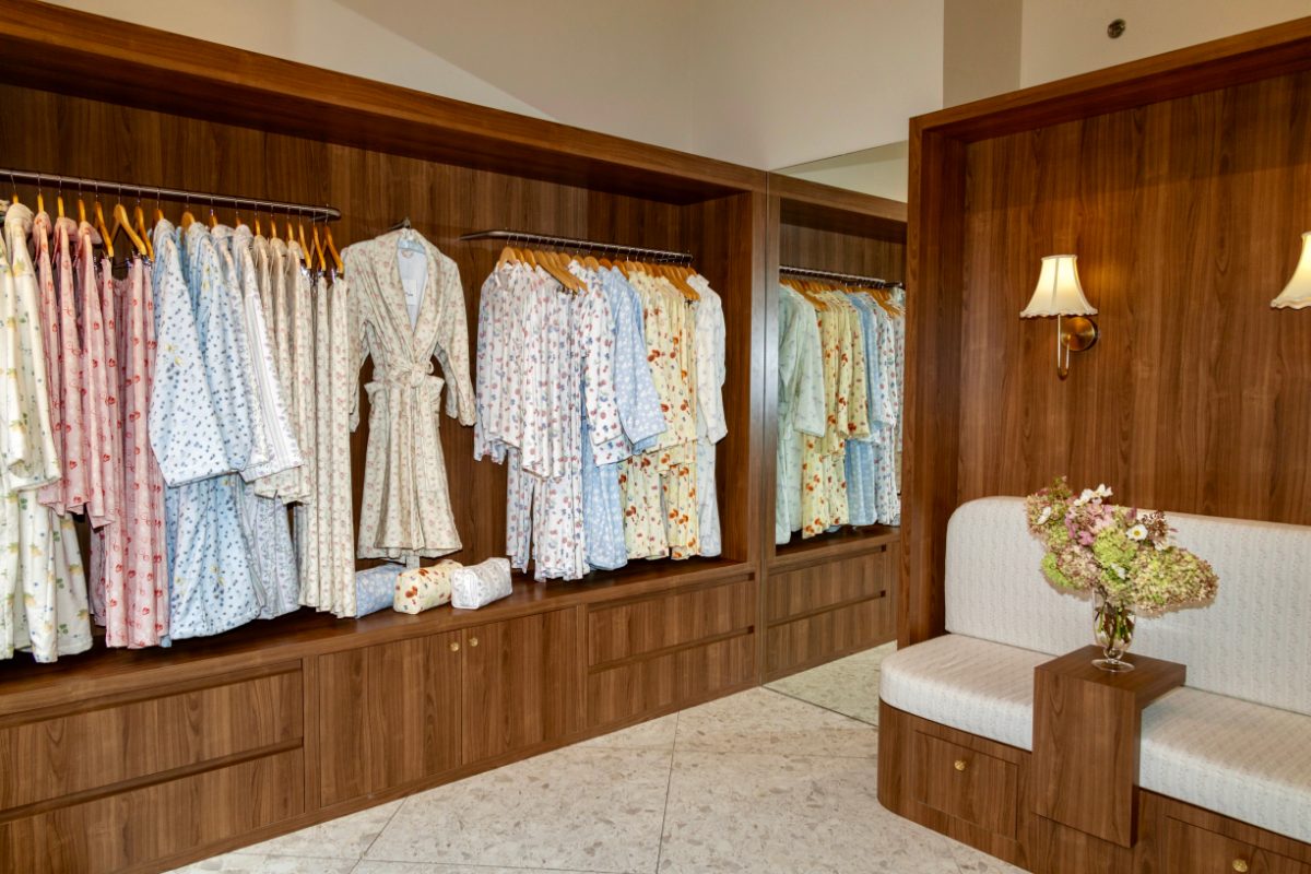 Collection of floral pajamas and robes on hangers in a wood closet with a bench.