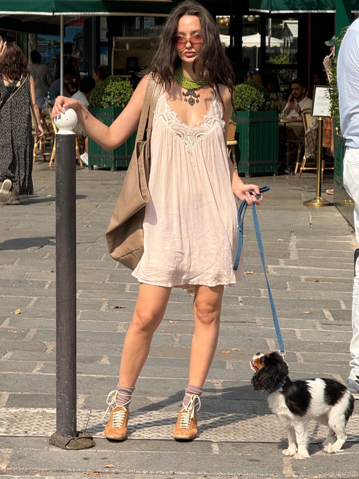 Blush pink boho dress with a chunky green necklace, brown bag, and dog on a leash.
