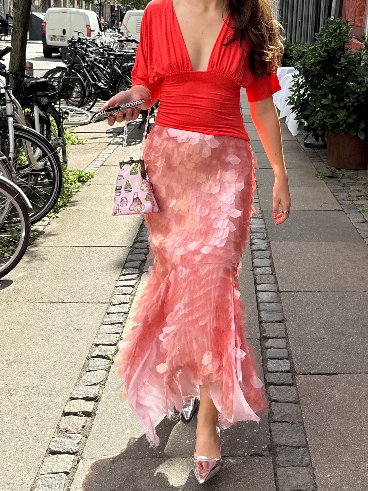 Coral deep-V top with a pink tiered skirt, silver heels, and a patterned clutch on a sidewalk.