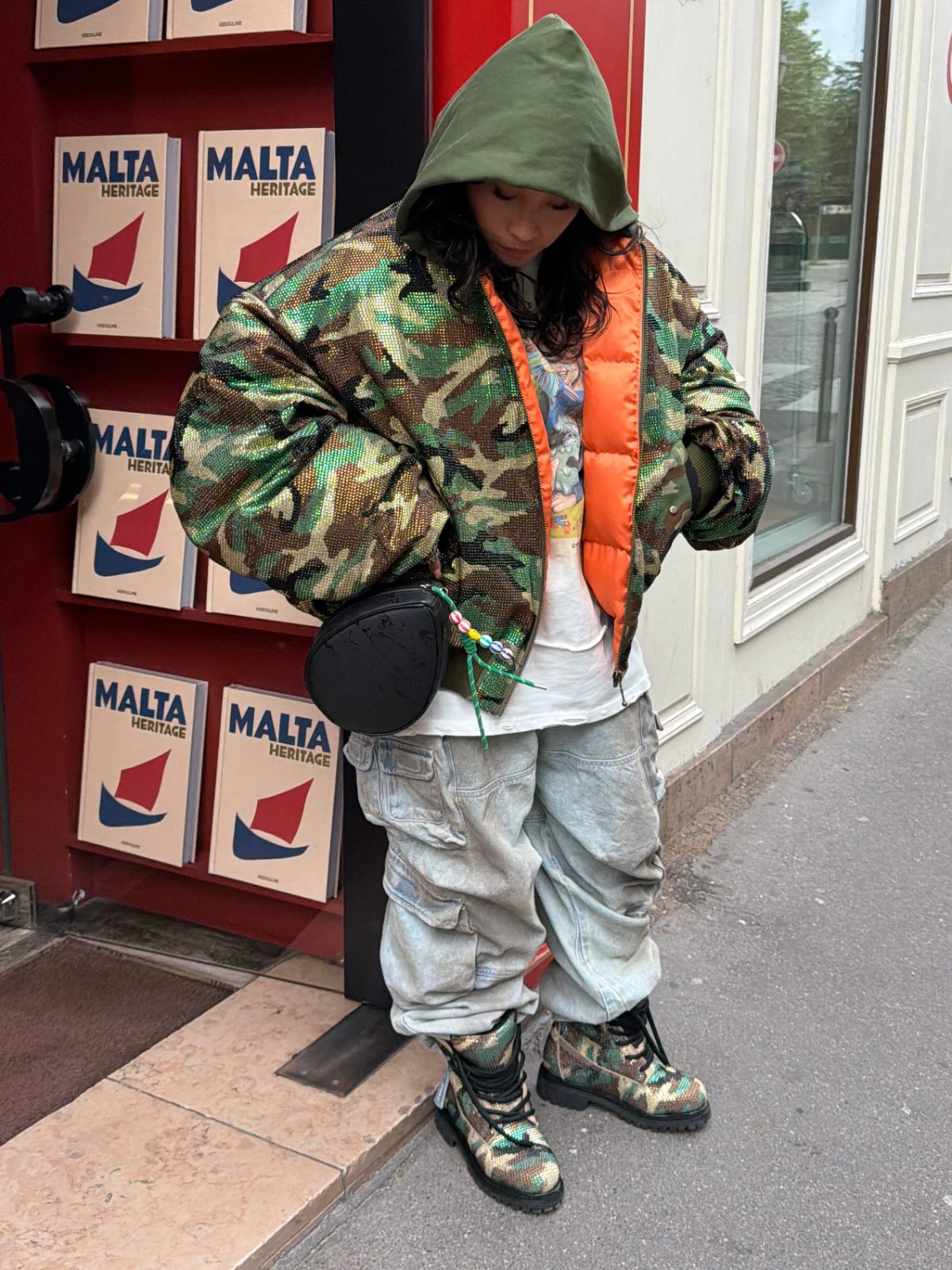 Green hooded camo sequin bomber jacket with orange lining, light wash cargo pants, and camo boots.