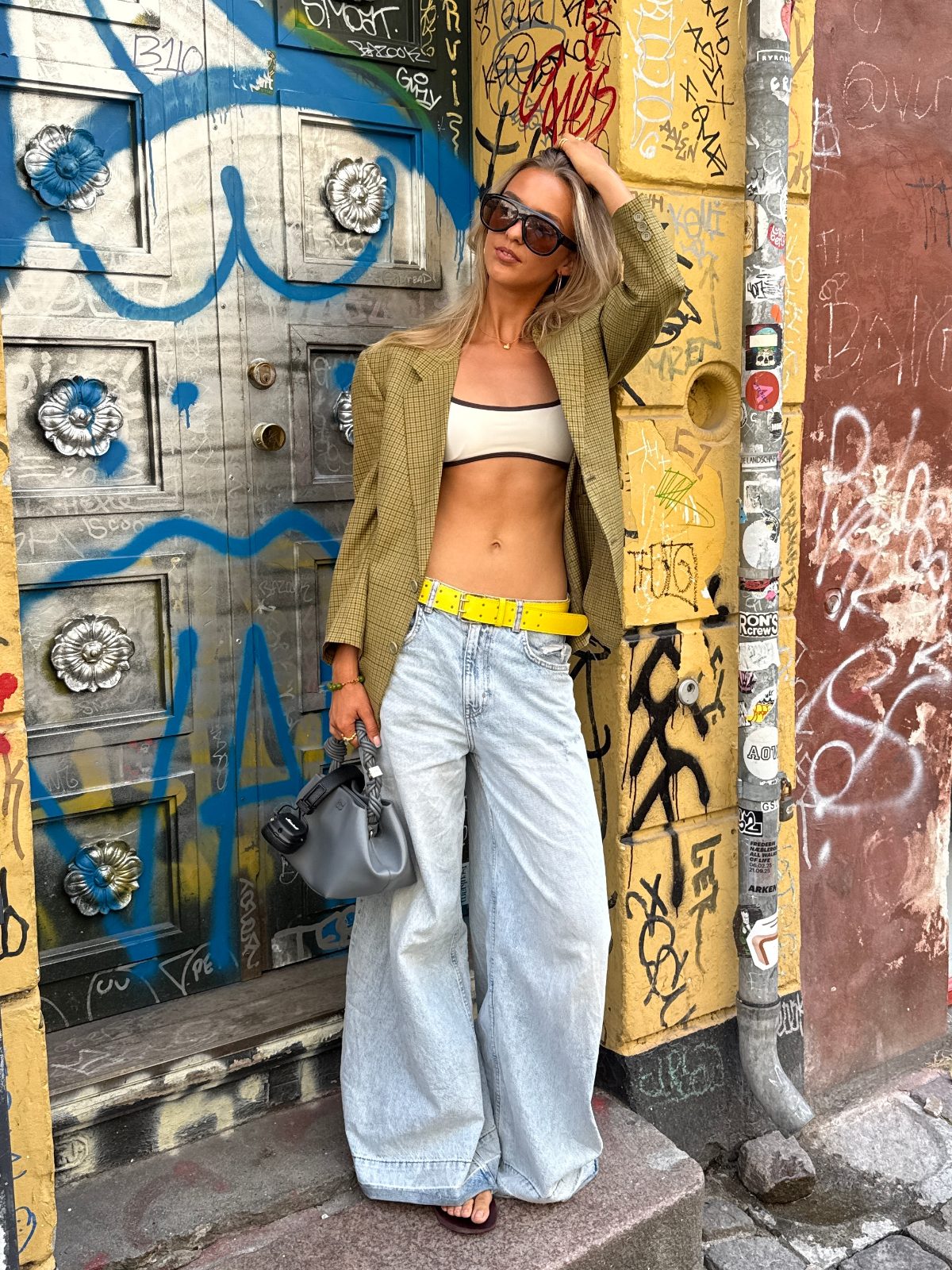 Plaid blazer, white bandeau top, wide-leg jeans, yellow belt, sunglasses, and gray bag.