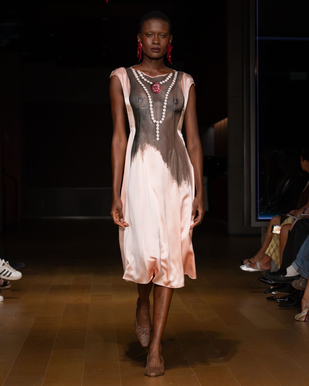 Pink slip dress with black brushstroke design, pearl necklace illusion, and red earrings.