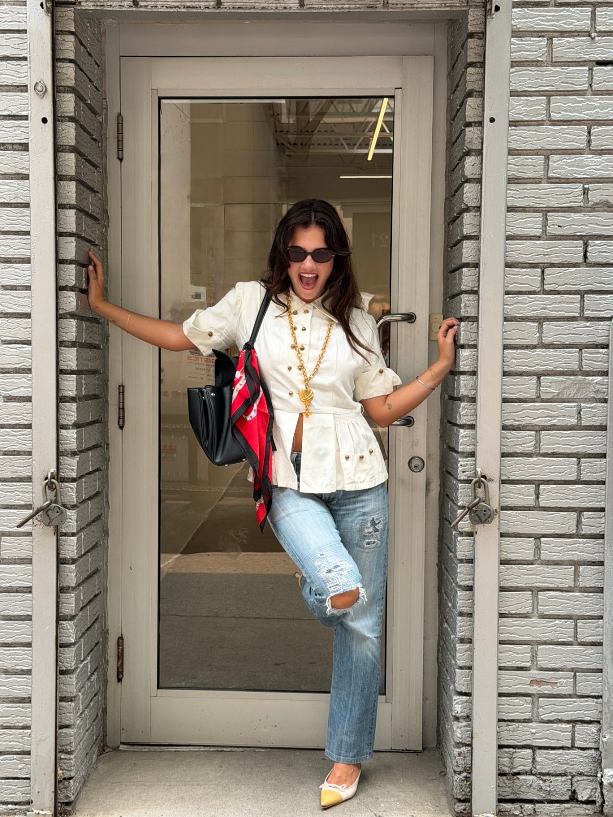 White button-up shirt with gold embellishments, distressed jeans, black bag, red scarf, and pointed flats.