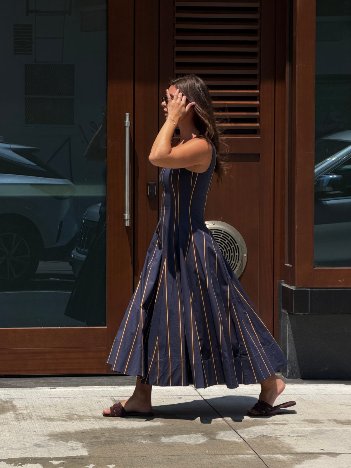 Navy striped sundress with sandals and sunglasses walking outside a building.