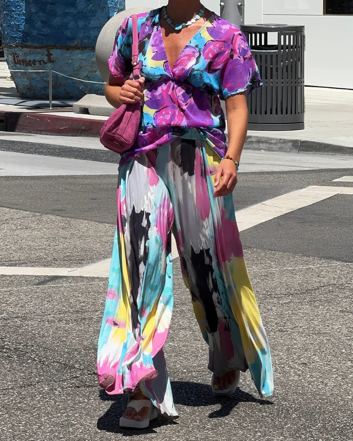 Colorful floral print top and wide-leg pants with a pink bag on a sunny street.