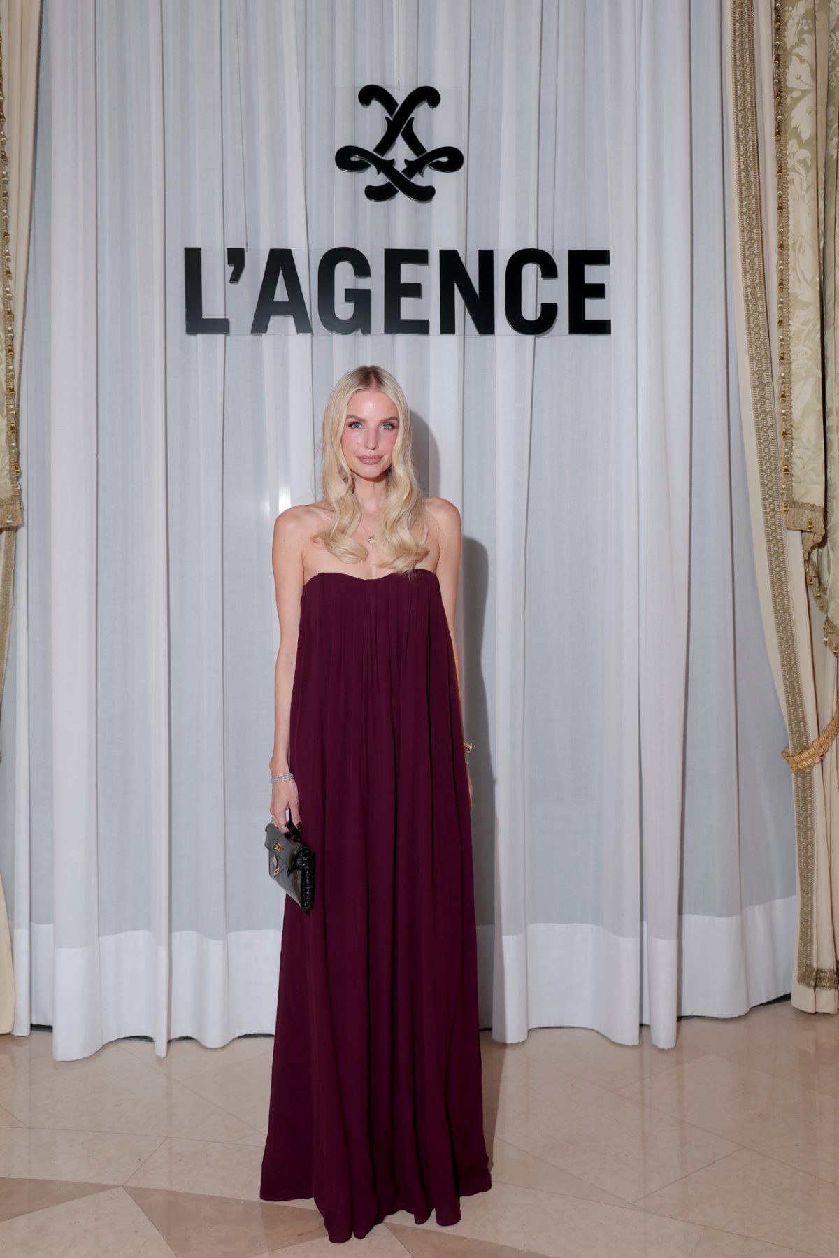 Burgundy strapless maxi dress with a black quilted clutch, standing in front of L'AGENCE logo.