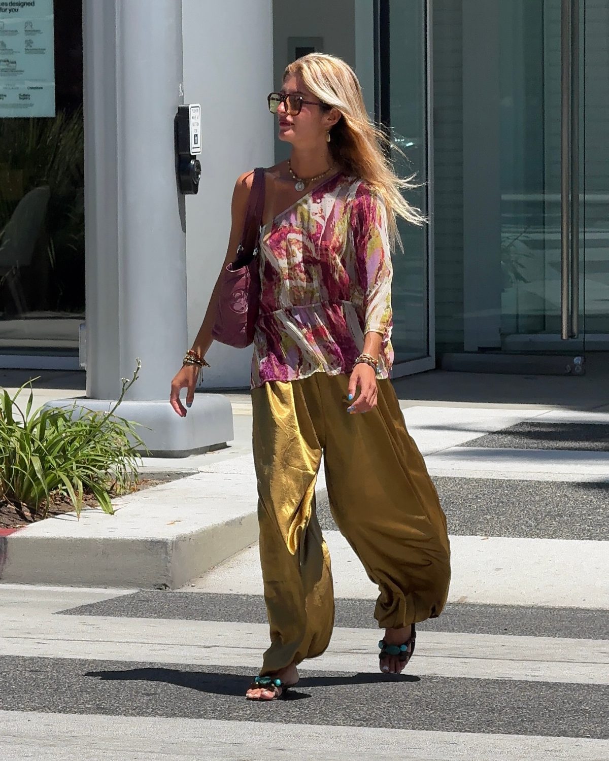 Floral one-shoulder top, gold satin wide-leg pants, and turquoise sandals on a sunny street.