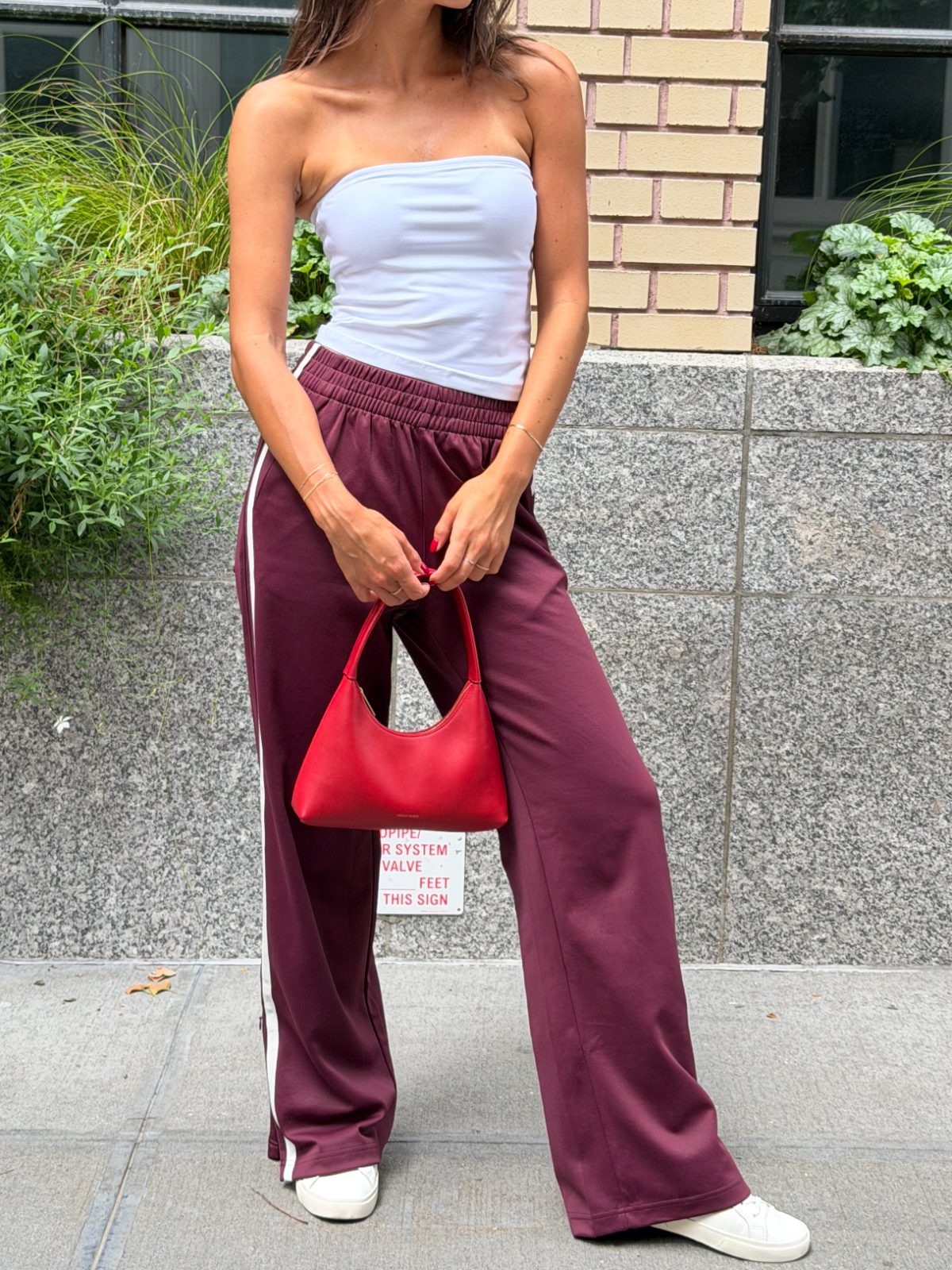 White strapless top with burgundy wide-leg pants, white sneakers, and a red handbag.