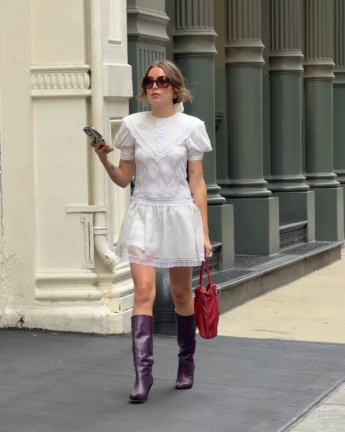 White lace puff-sleeve top and mini skirt, with purple knee-high boots and a red bag.