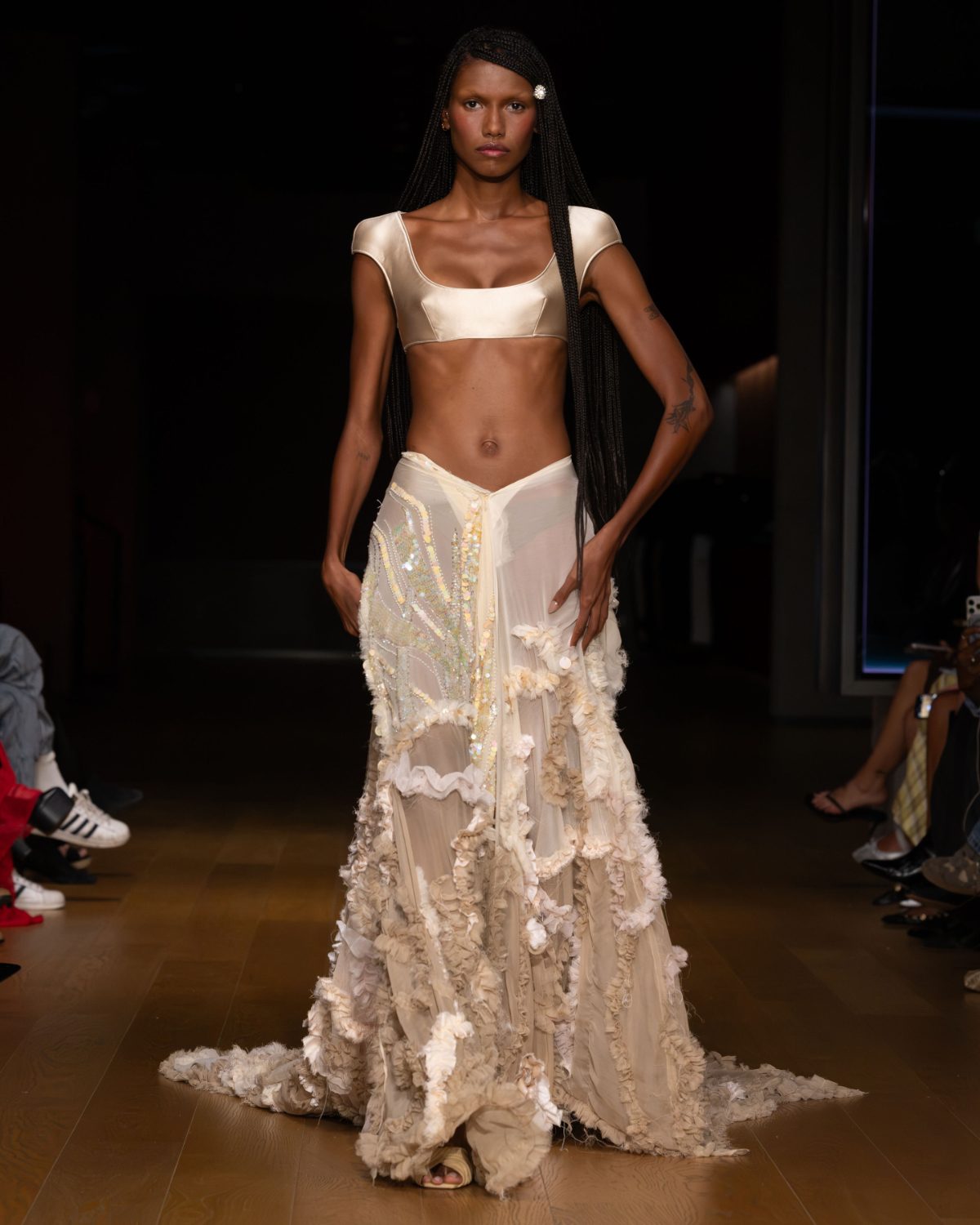 Cream satin bra top and sheer ruffled skirt with sequins on a runway.