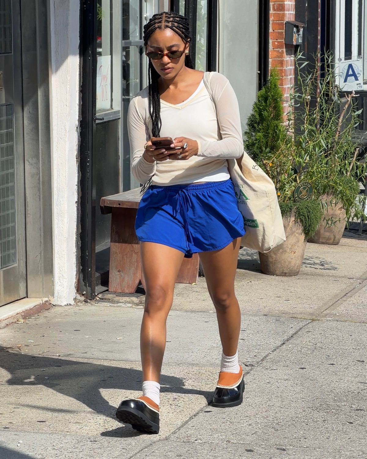Summer street style featuring a beige long-sleeve top, blue shorts, and platform clogs.