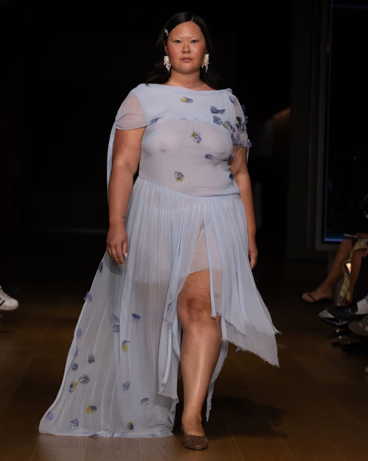 Light blue sheer dress with floral appliques and a high slit, worn with pearl earrings.
