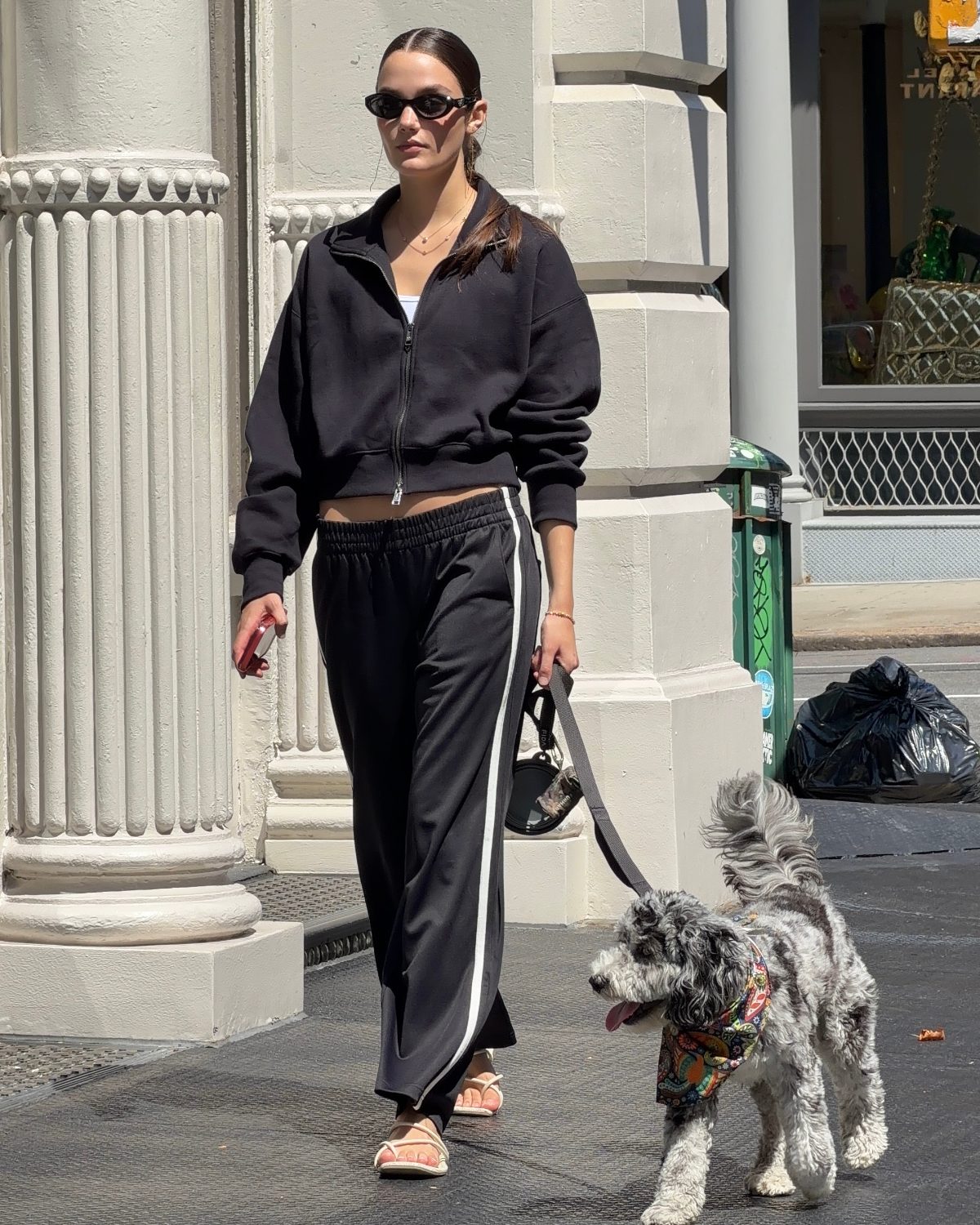 Black zip-up hoodie, black track pants with white stripe, and sandals on a sunny street with a dog.