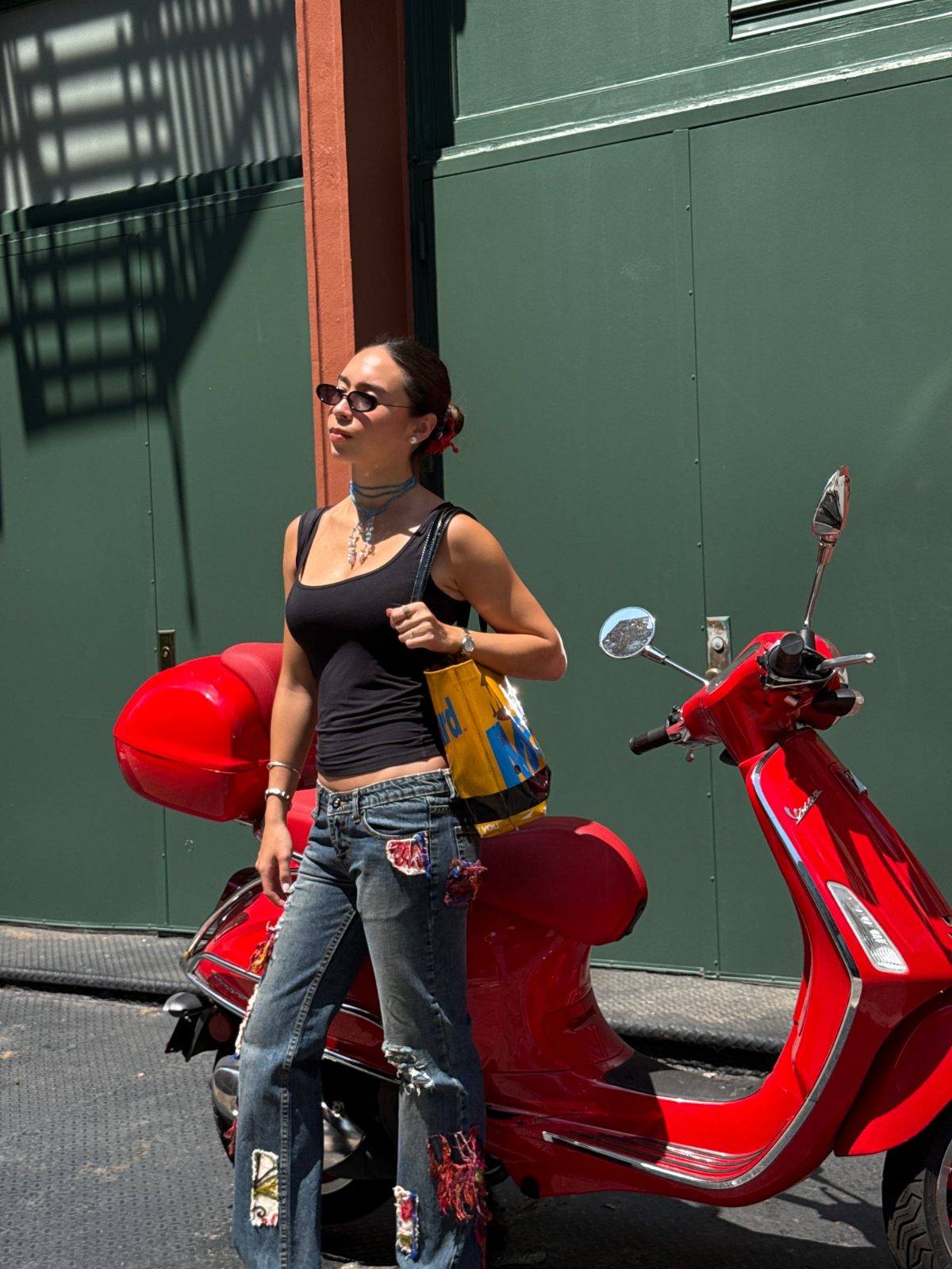 Black tank top, patched jeans, and sunglasses with a red Vespa scooter.