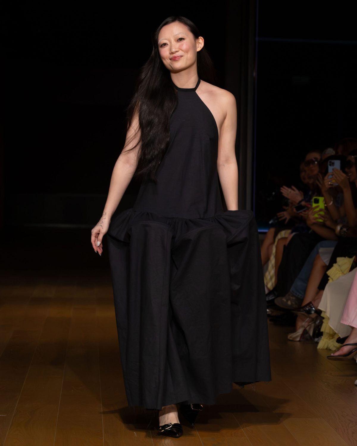 Black halter-neck dress with balloon skirt and black buckled heels on a runway.