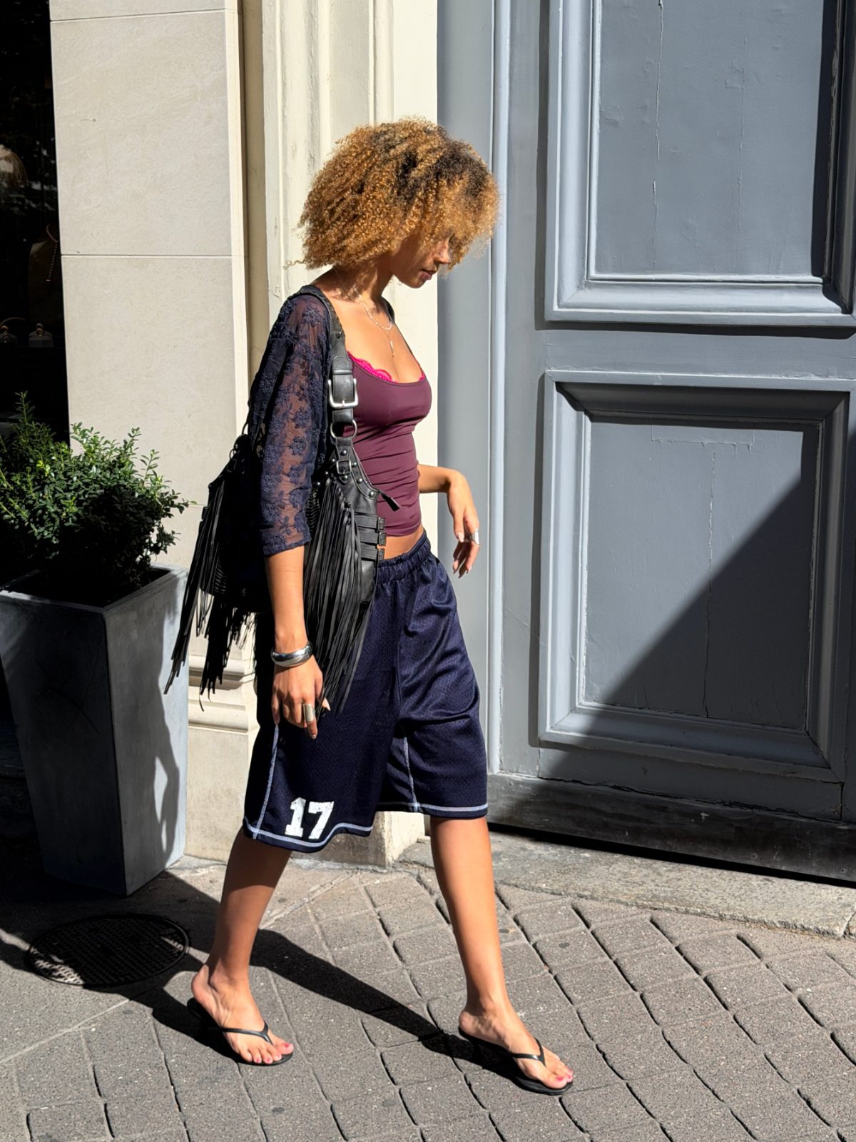 Burgundy tank top, navy athletic shorts, sheer lace shrug, and black fringe bag.