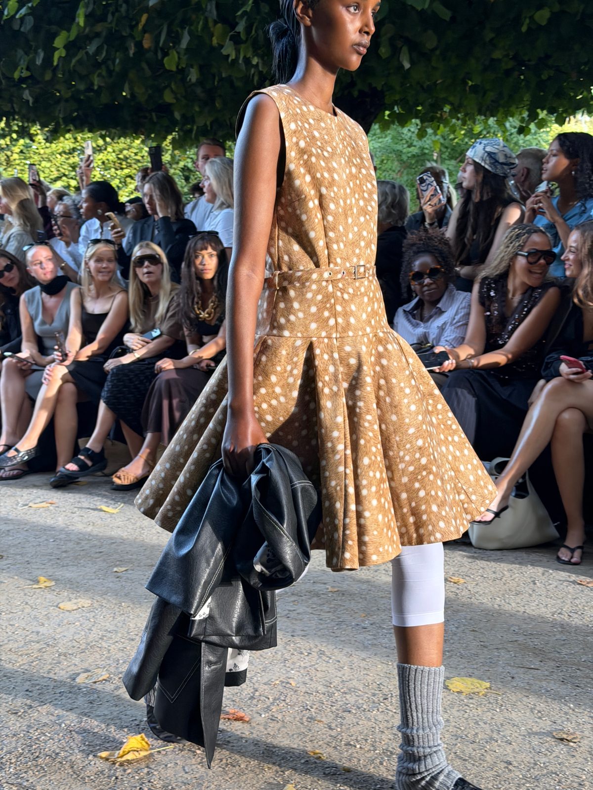 Fawn-print pleated mini dress with white leggings, grey leg warmers, and a black jacket.