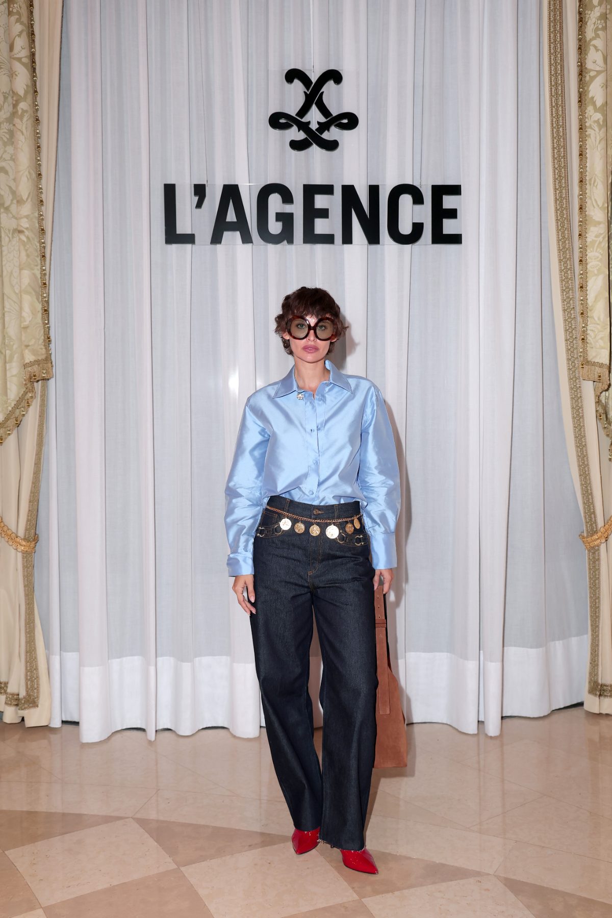 Light blue button-up shirt, dark denim jeans with coin belt, and red pointed-toe heels.