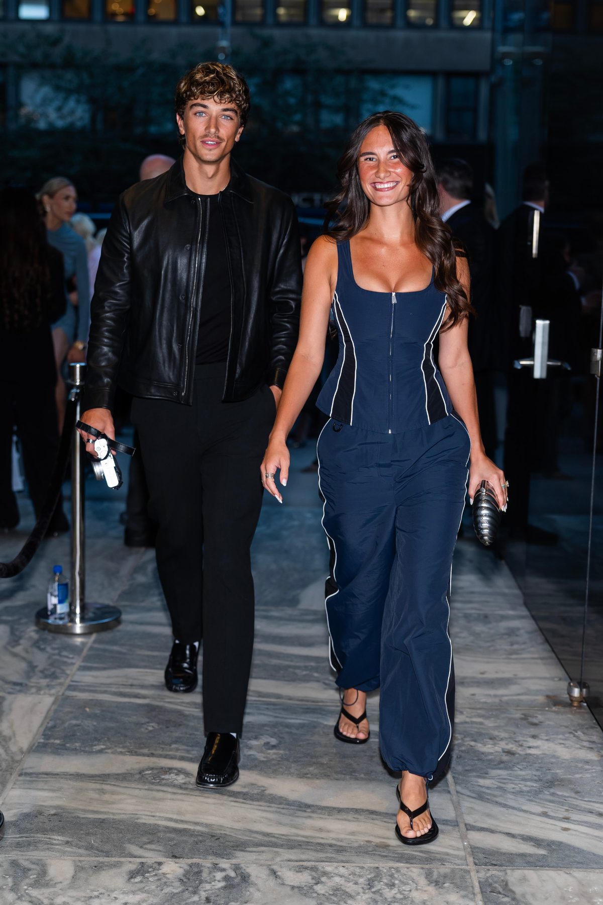 Black leather jacket, black tee, and black trousers with a navy jumpsuit with white stripes.