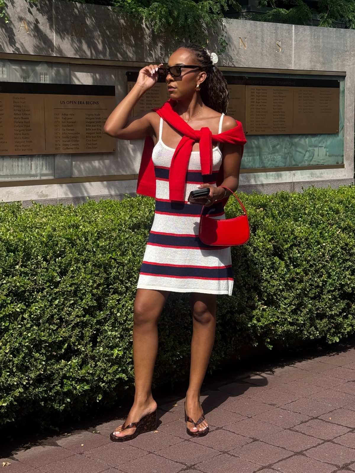 White and navy striped knit dress, red sweater, red purse, and tortoise shell wedge flip-flops.