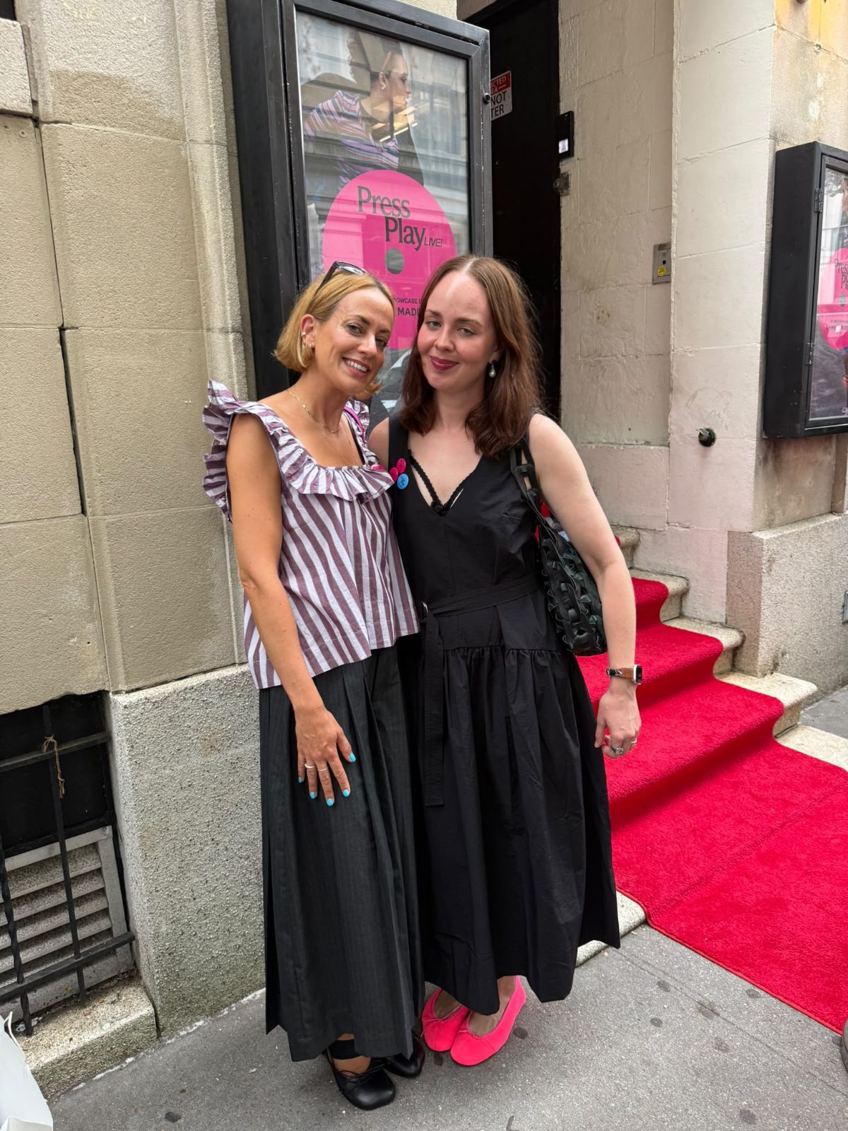 Two women in stylish outfits on a red carpet outside a building.