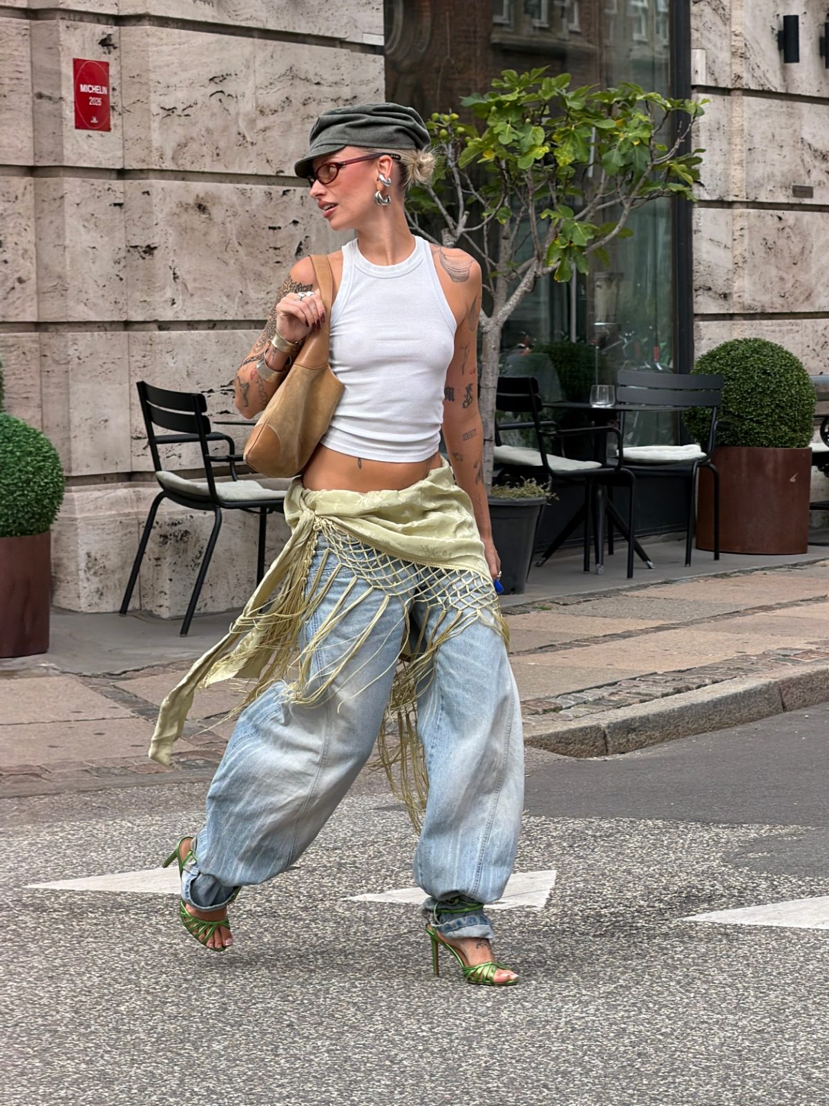 White ribbed tank top, baggy acid wash jeans with a fringed wrap skirt, and green heels.