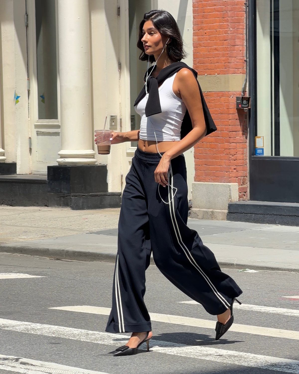 White ribbed crop top, navy wide-leg track pants, black heels, and a sweater over shoulders.