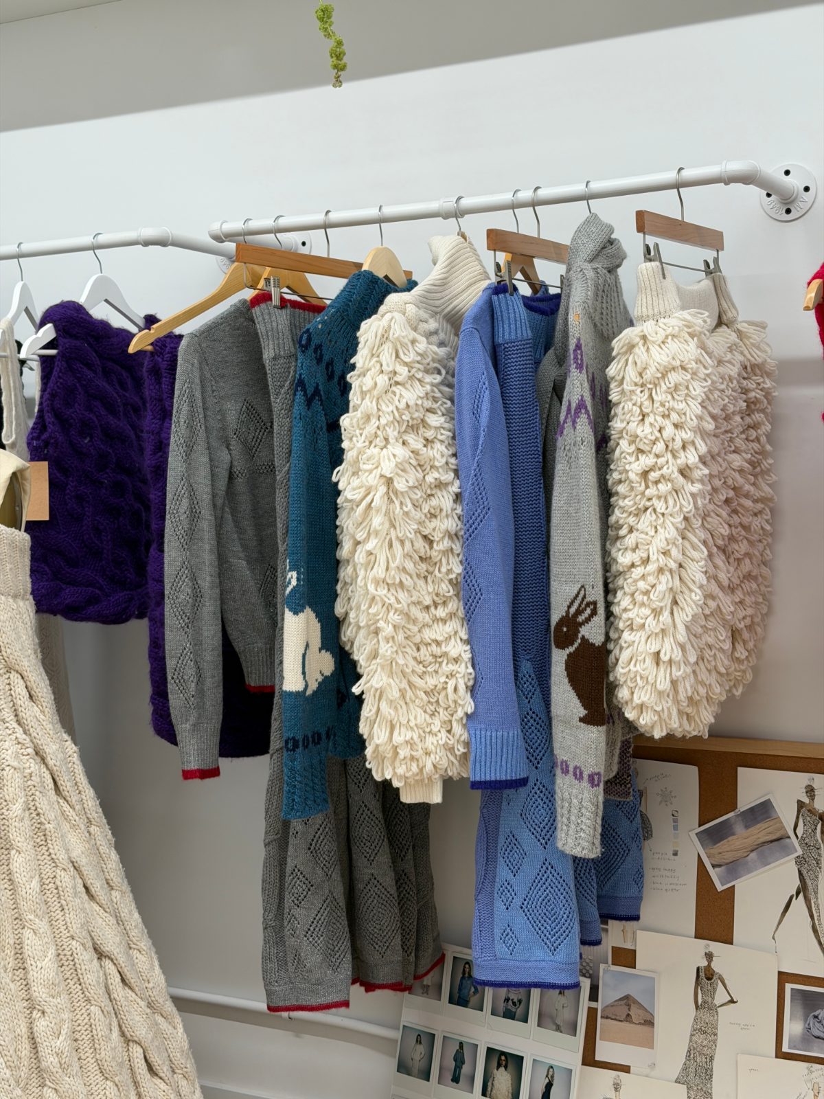Variety of knit sweaters in purple, grey, blue, and cream hanging on a rack.
