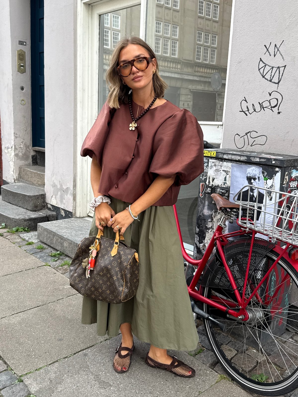 Brown puff-sleeve top, olive midi skirt, mesh flats, and a Louis Vuitton bag.