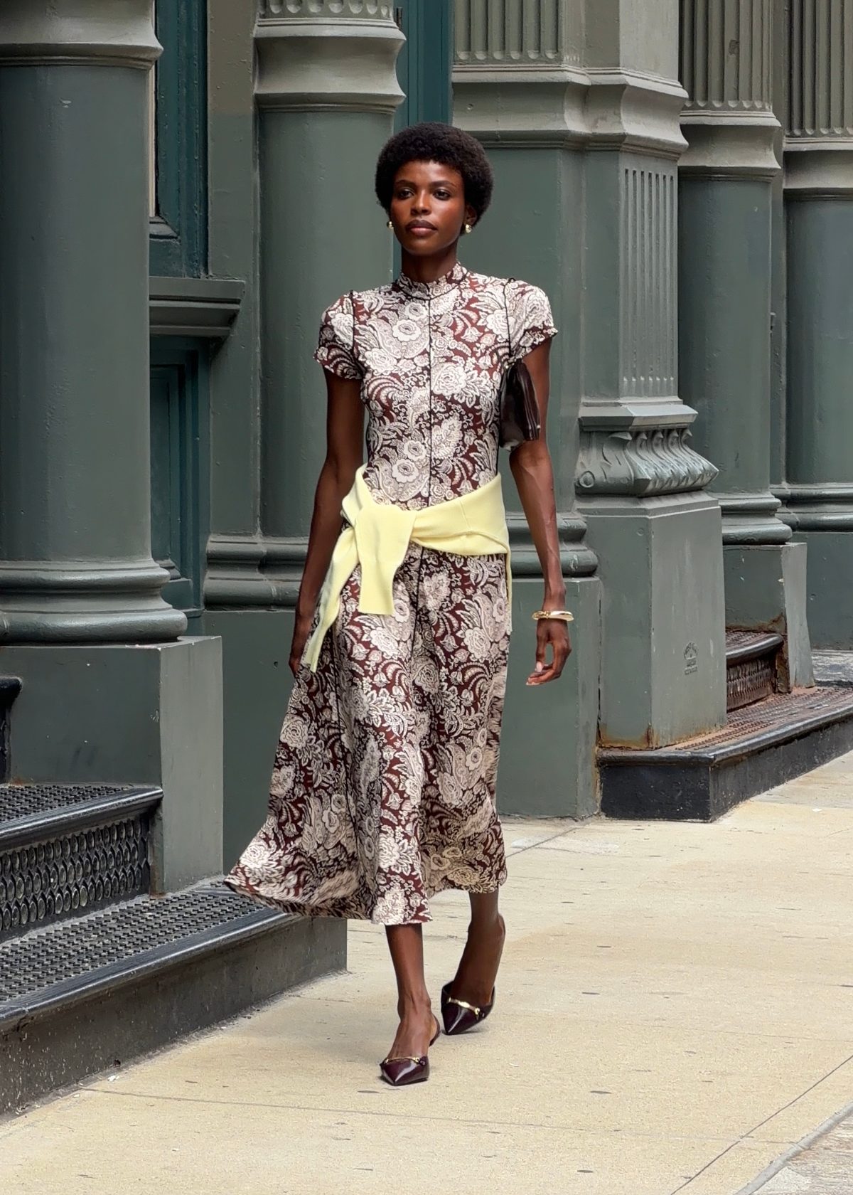 Brown and white floral midi dress with a yellow sweater tied at the waist.