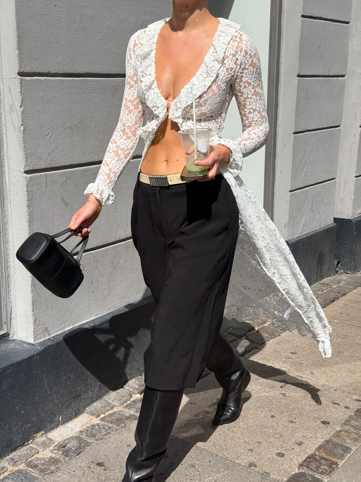 White ruffled lace crop top, black wide-leg pants, black boots, and a matching bag.