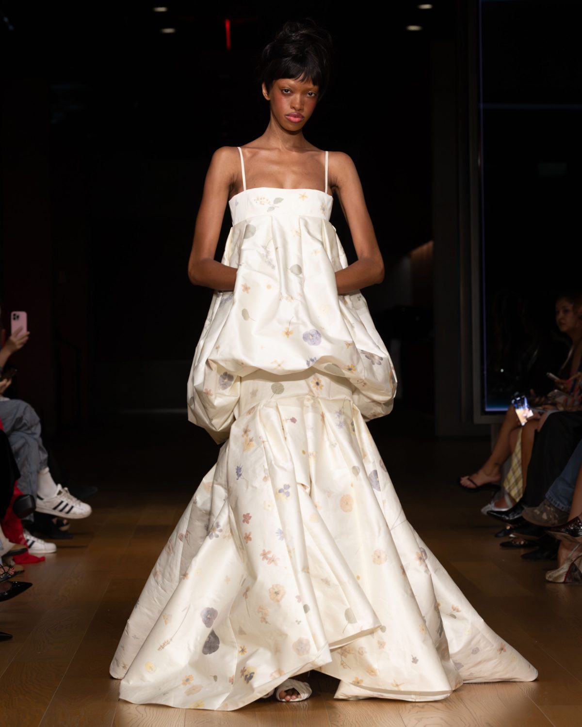 White floral print gown with spaghetti straps and voluminous tiered skirt on a runway.