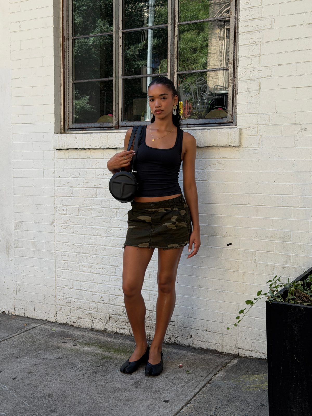 Black tank top with olive green camo mini skirt, black split-toe flats, and round black bag.