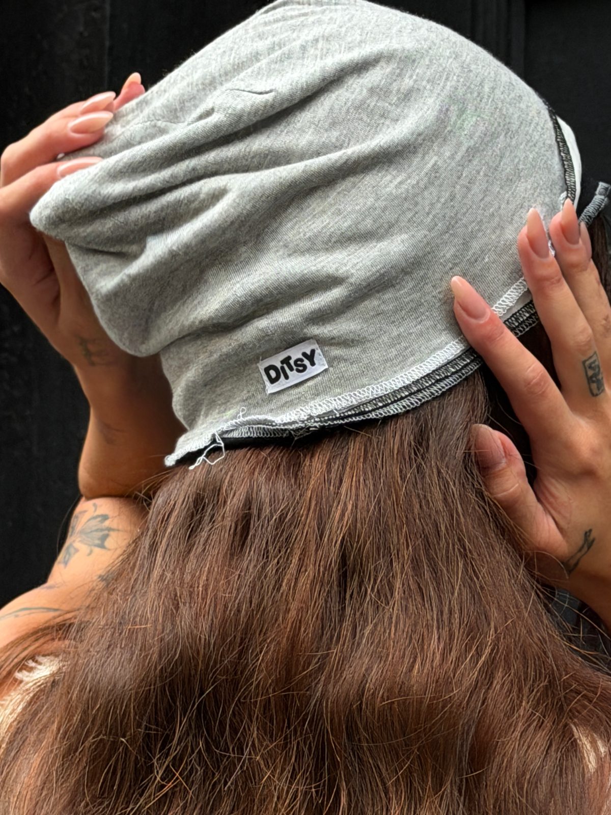 Gray Ditsy beanie being adjusted on a head with brown hair and tattoos.