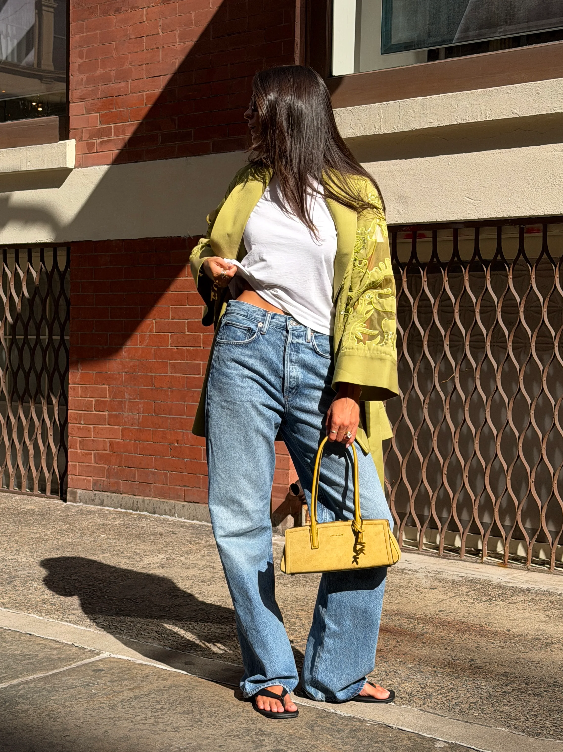 Olive green embroidered jacket, white tee, baggy jeans, black sandals, yellow handbag.