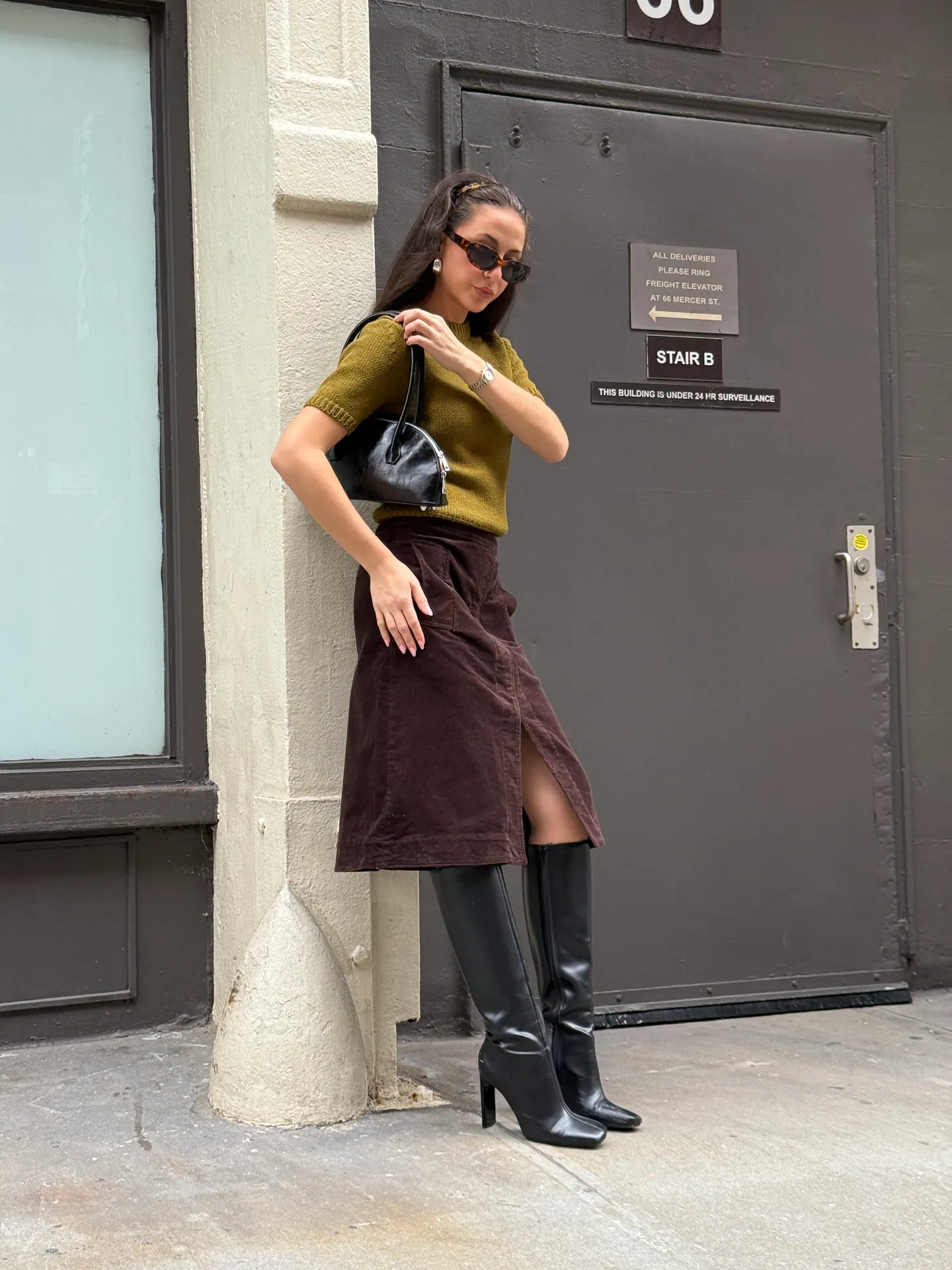 Olive knit top, brown corduroy midi skirt with slit, black knee-high boots, and black handbag.