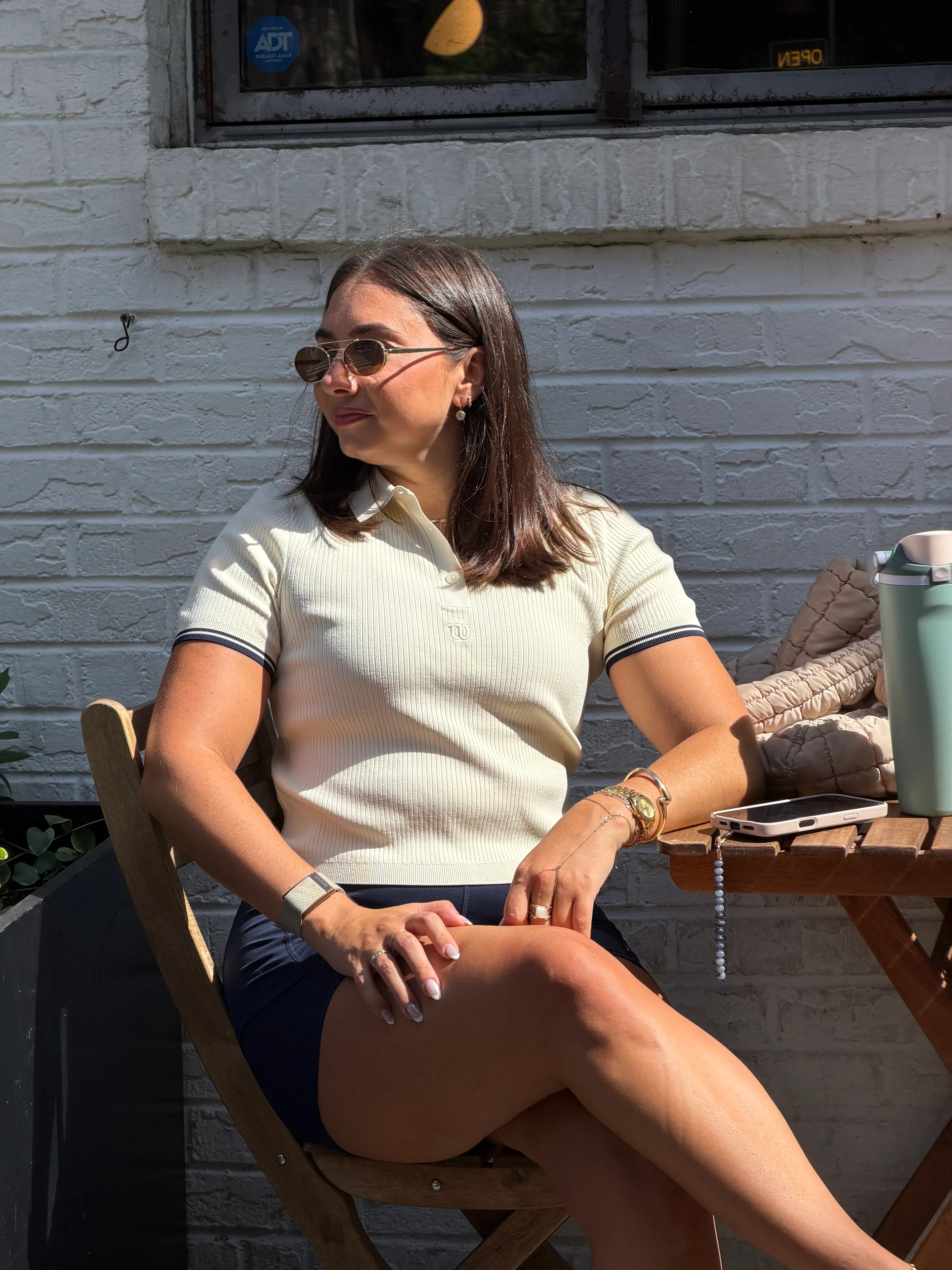 Cream ribbed polo shirt with navy trim and dark shorts, brown sunglasses.