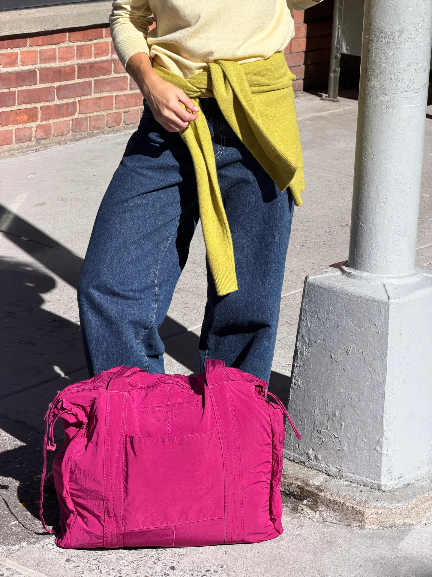 Cream sweater, wide-leg jeans, yellow sweater tied at waist, and hot pink duffel bag.