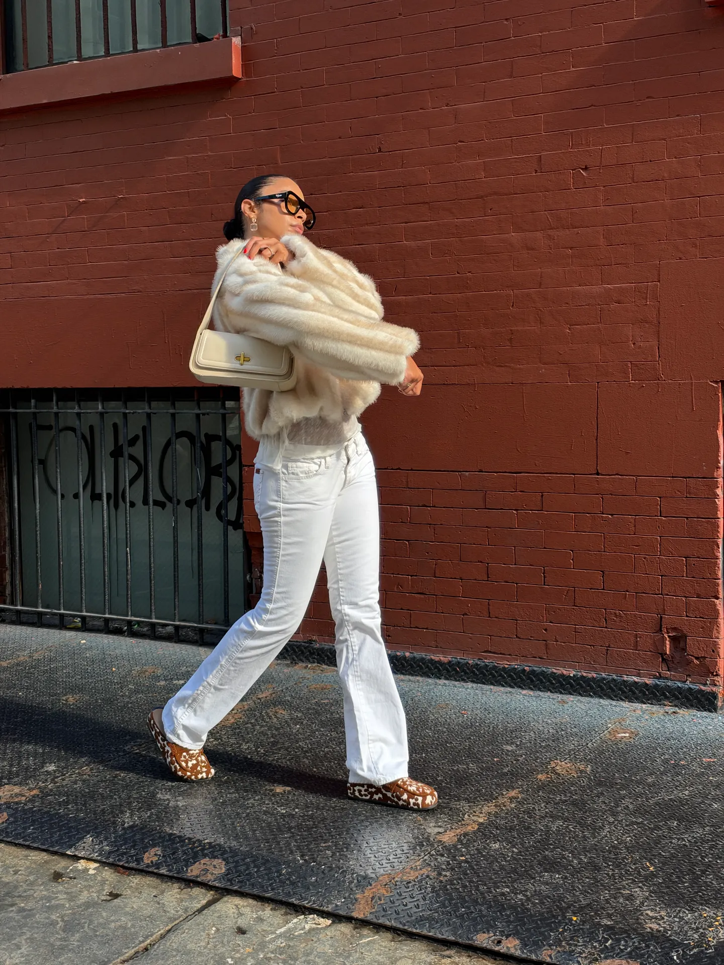 White faux fur jacket, white flared jeans, cow print shoes, cream shoulder bag.