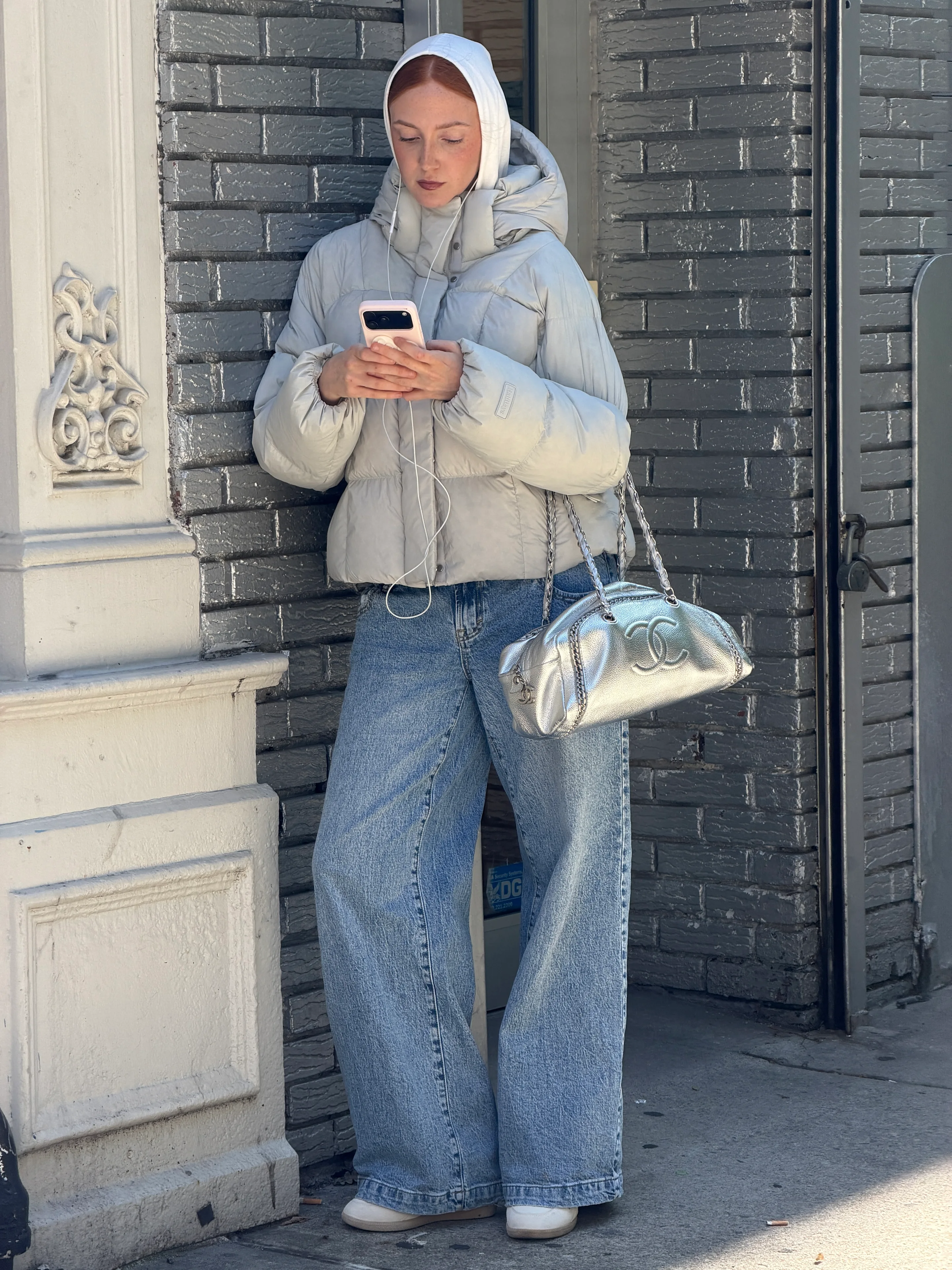 Light gray puffer jacket, wide-leg jeans, white shoes, and a silver Chanel bag.