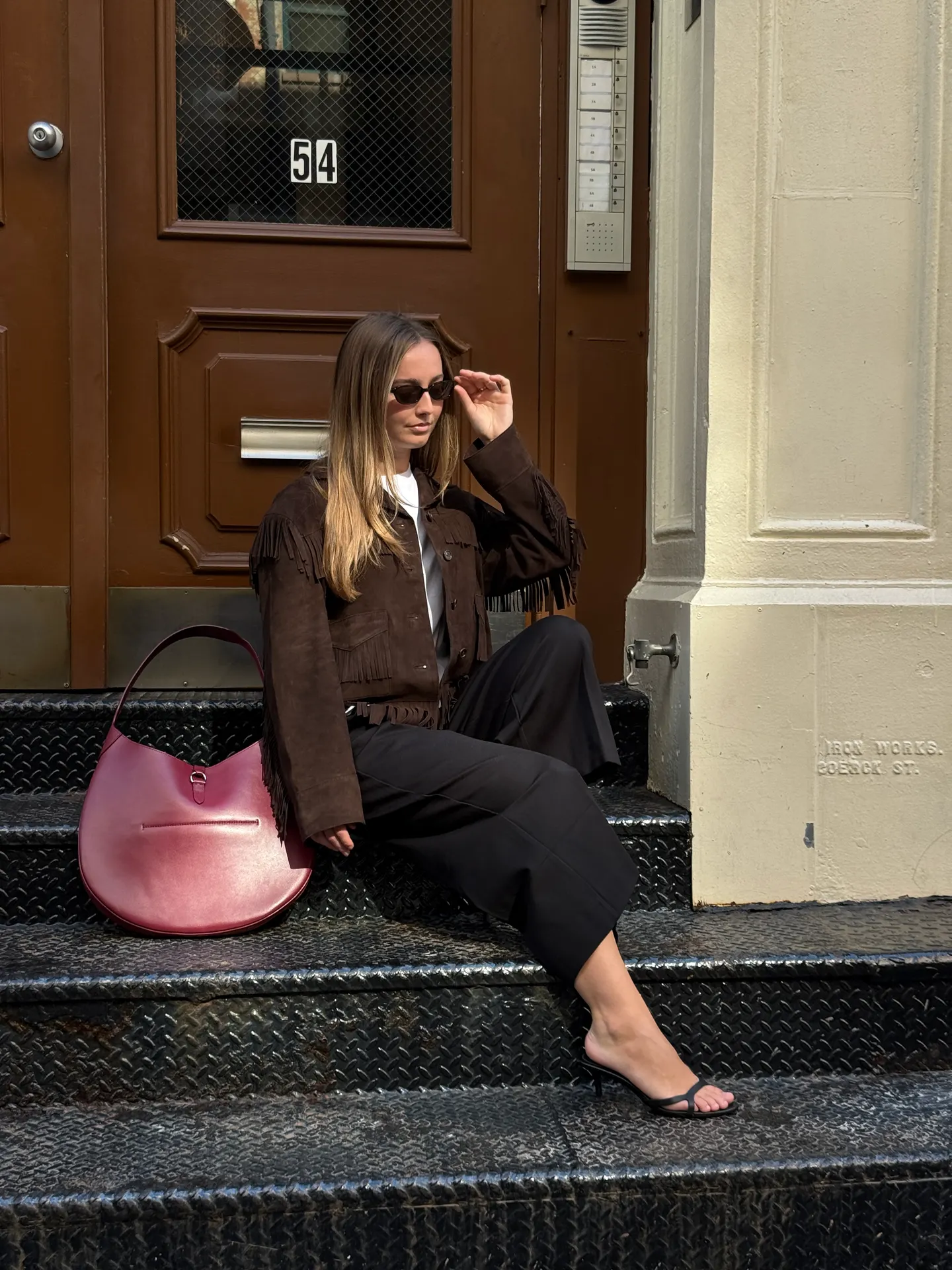 Brown fringe jacket, black wide-leg pants, and red shoulder bag on black steps.