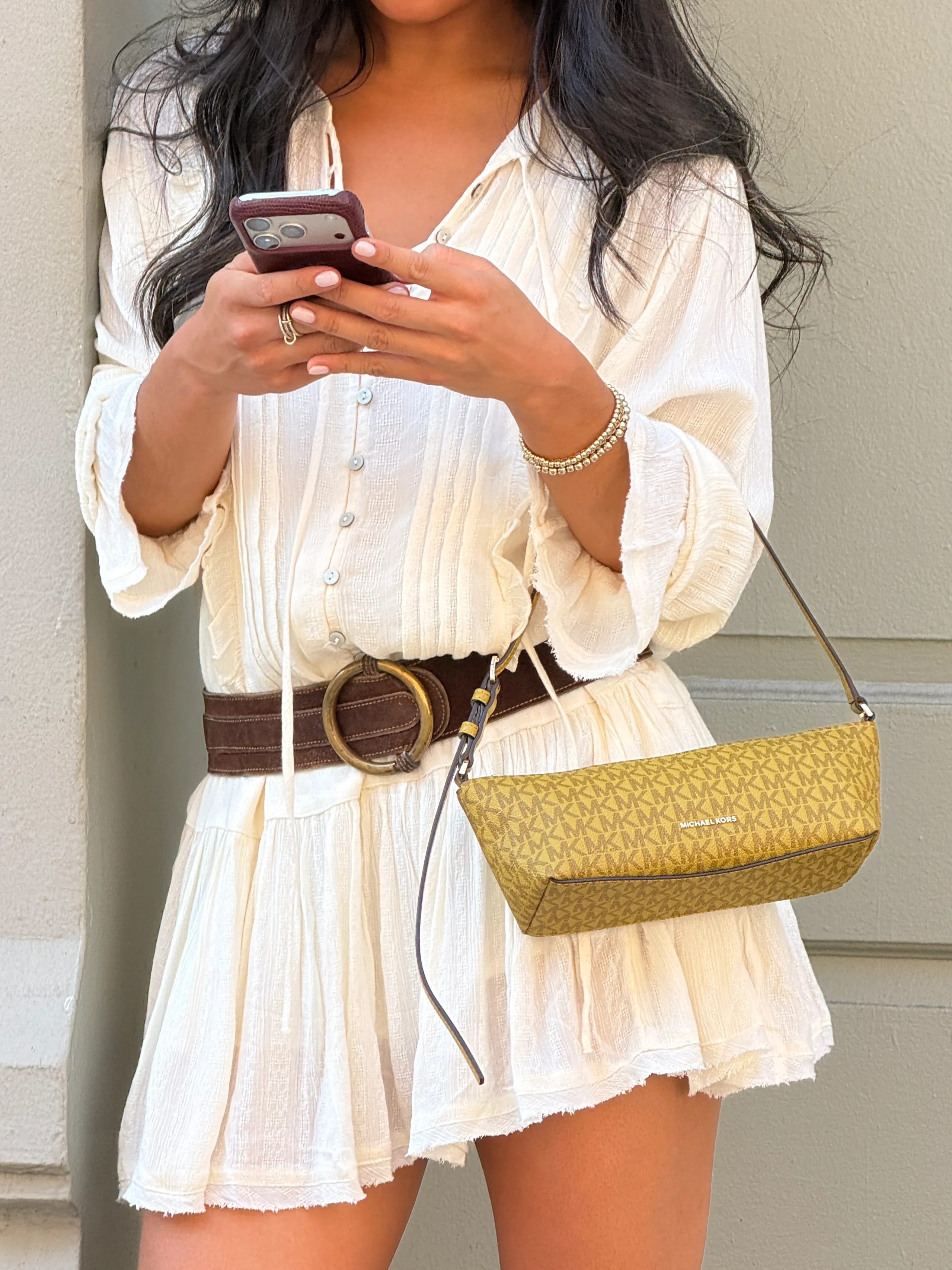 White textured tunic dress with a brown belt, beaded bracelets, and a patterned Michael Kors bag.