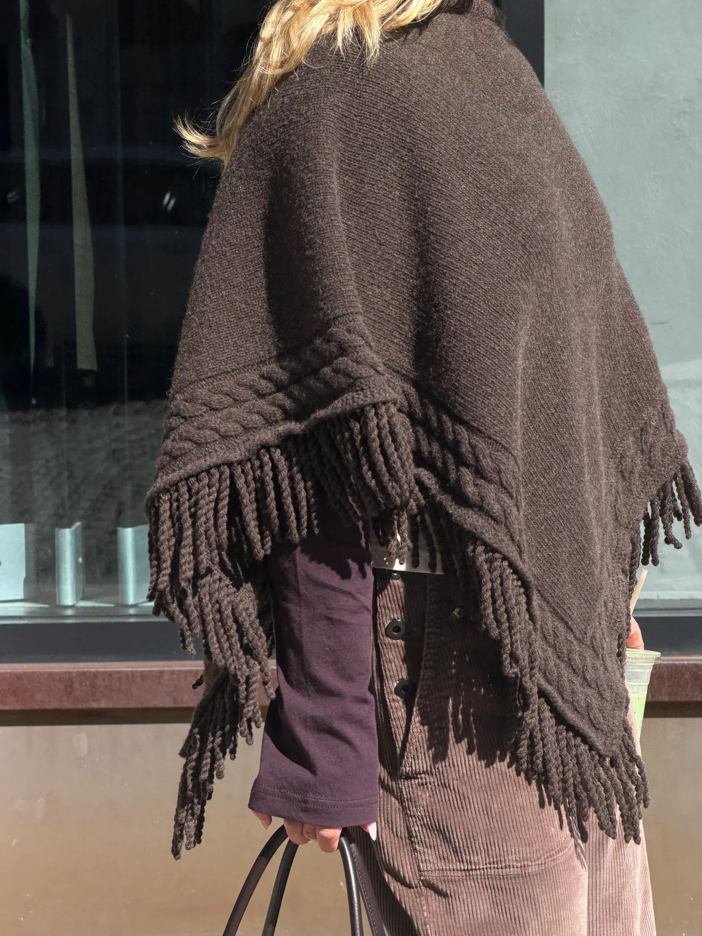 Brown knit poncho with fringe and cables over purple top and corduroy.
