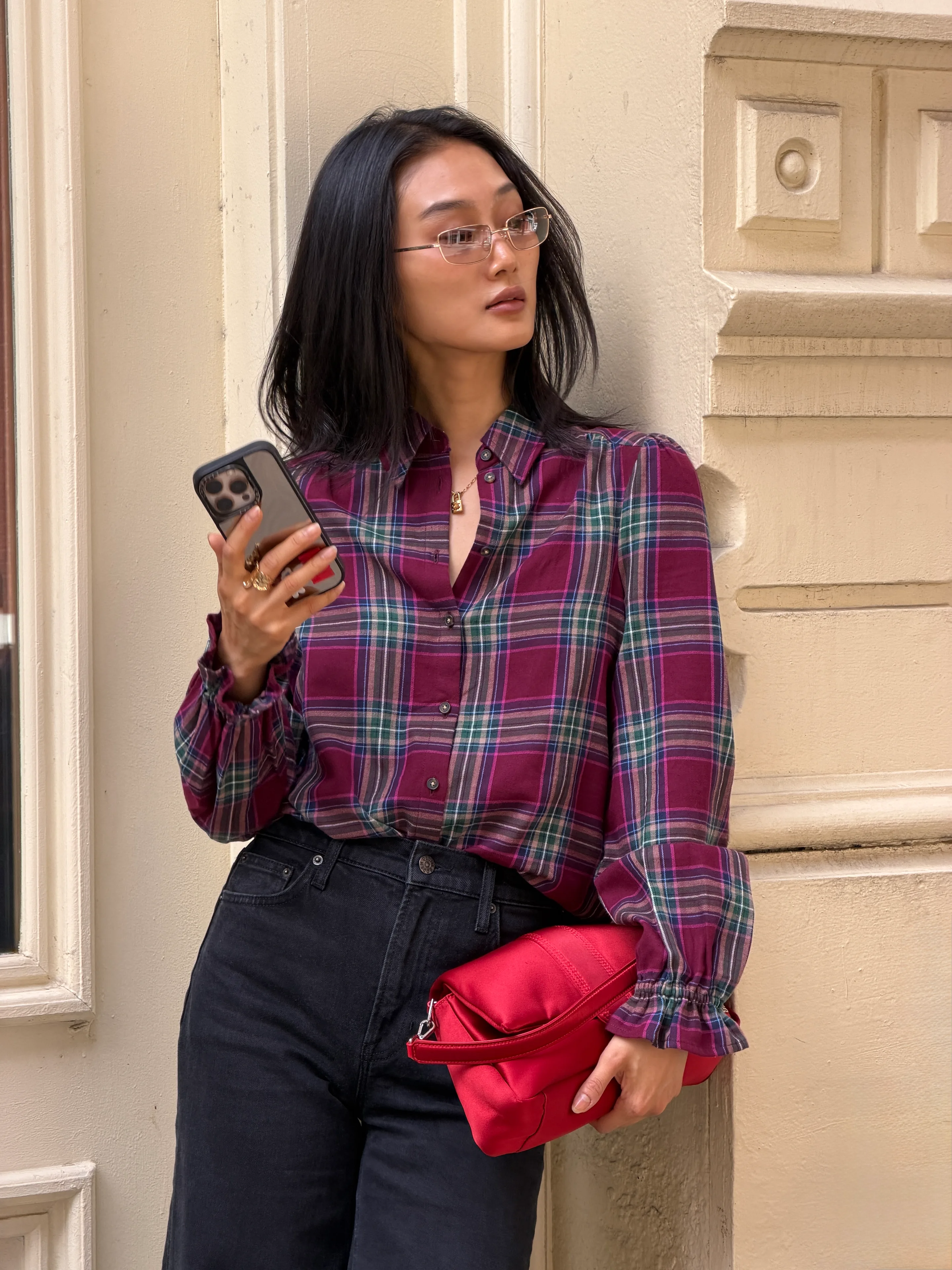 Plaid button-up shirt in red, green, and blue with black wide-leg jeans and a red clutch.