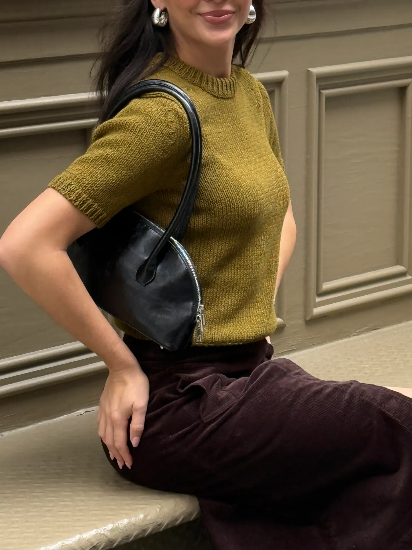 Olive green knit top with brown corduroy pants, black handbag, and silver hoop earrings.