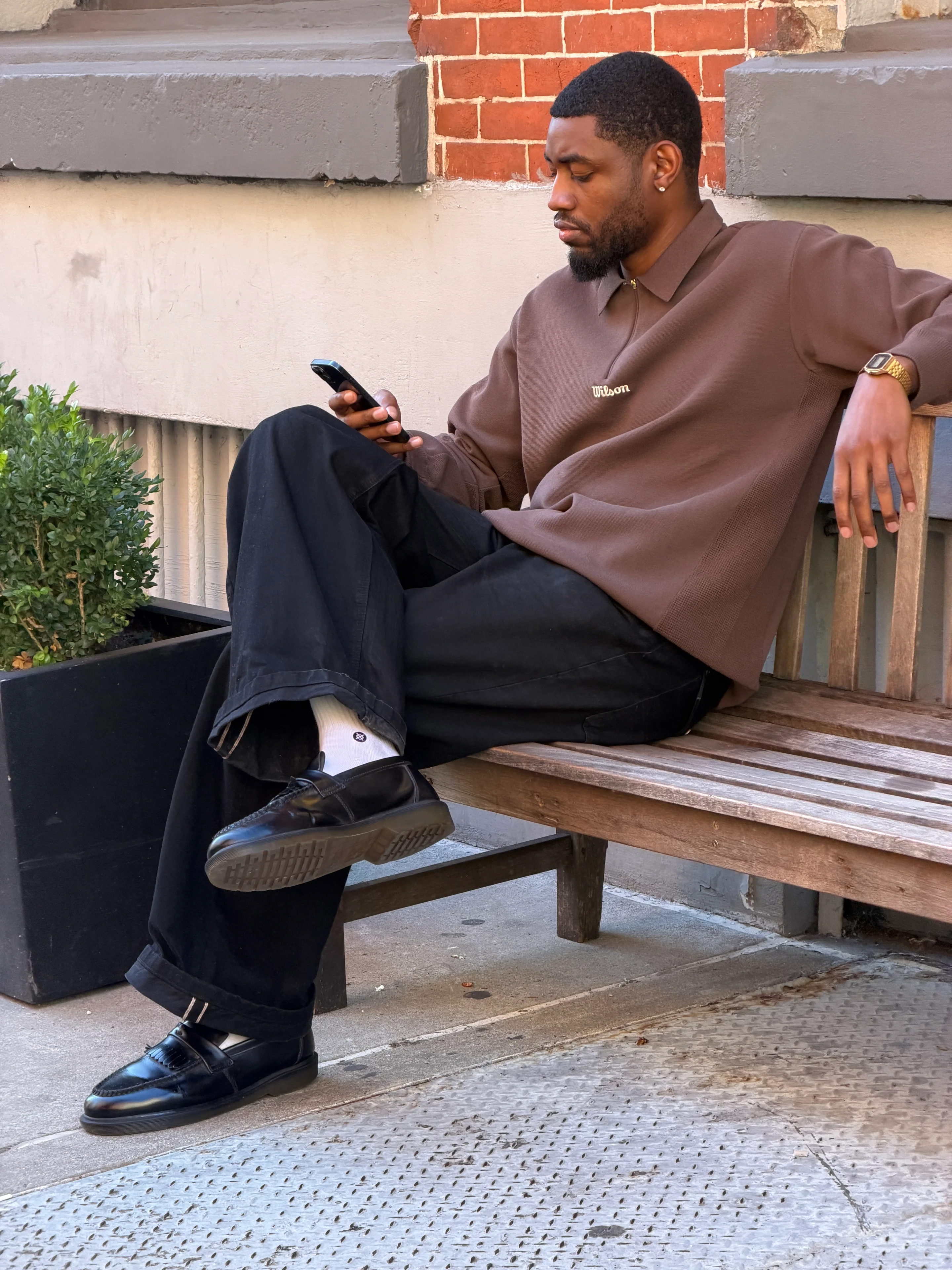 Brown collared sweatshirt with Wilson logo, black wide-leg pants, and black tasseled loafers.