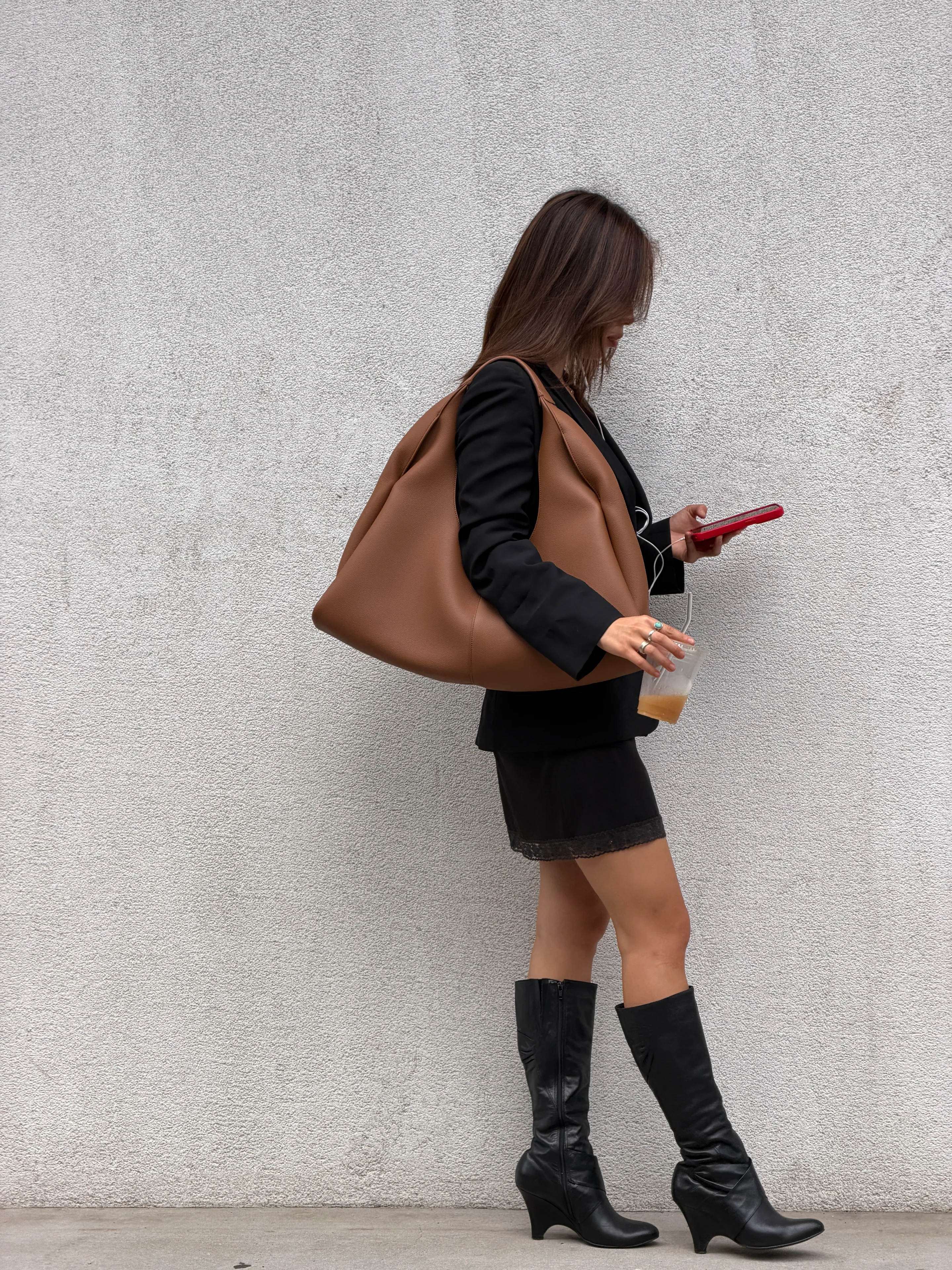 Black blazer over lace slip dress, brown hobo bag, black boots, red phone, and iced coffee.