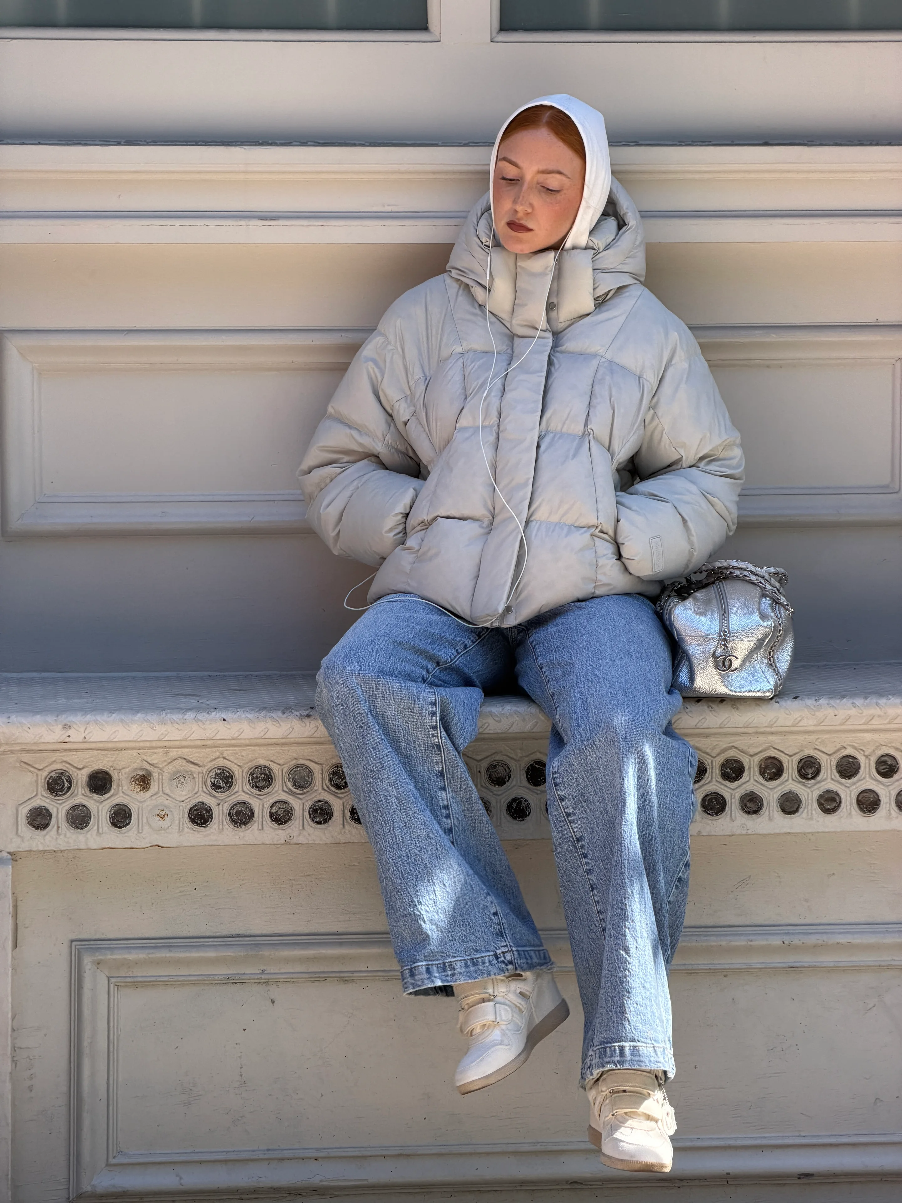Light gray puffer jacket, baggy jeans, white sneakers, and a silver bag.